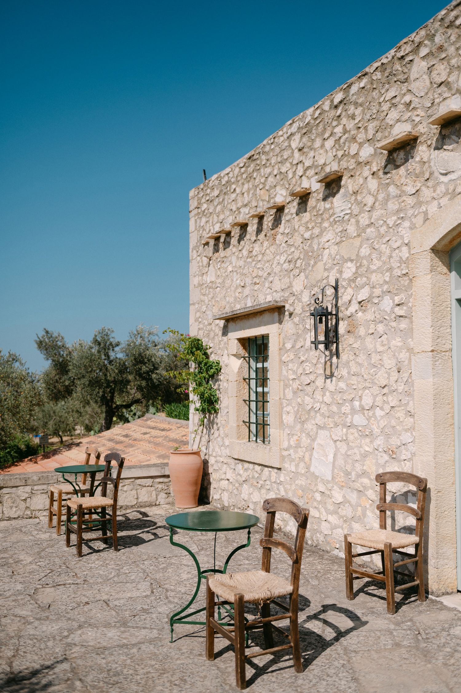 Stone patio with wooden chairs and metal table outside rustic Agreco Farms showcasing traditional architecture.