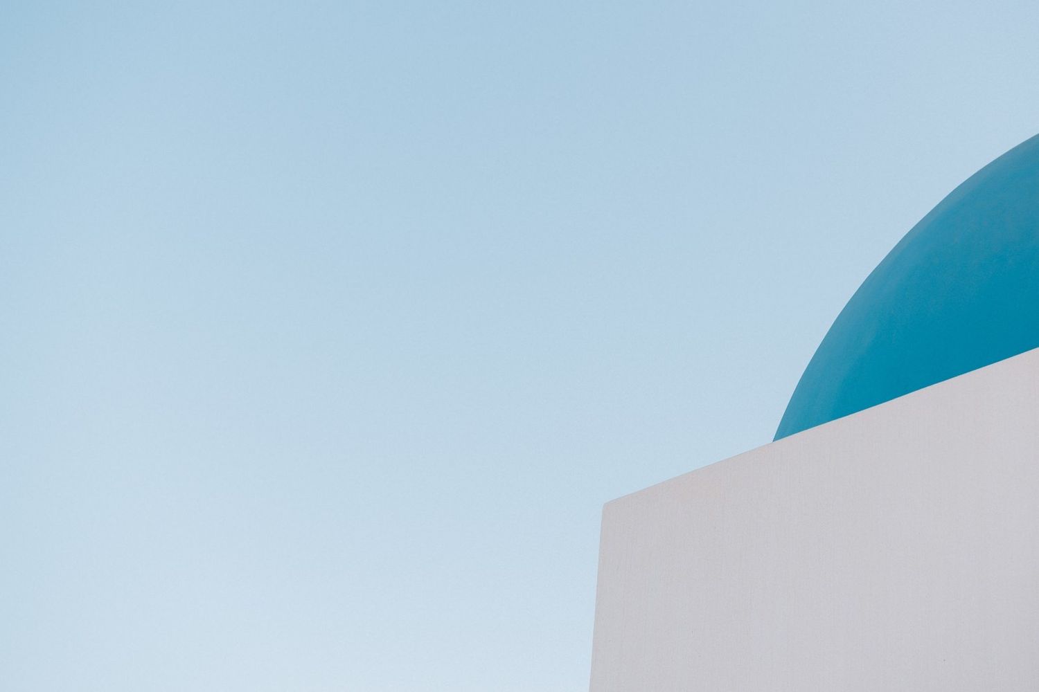 A bright blue dome against white architecture and clear sky in Santorini.