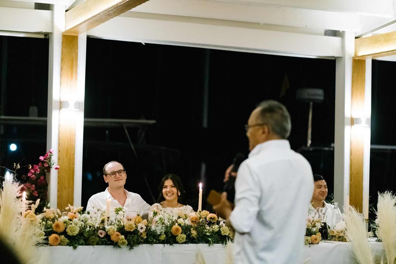 Wedding reception dinner setup with elegant floral centerpieces and warm lighting.