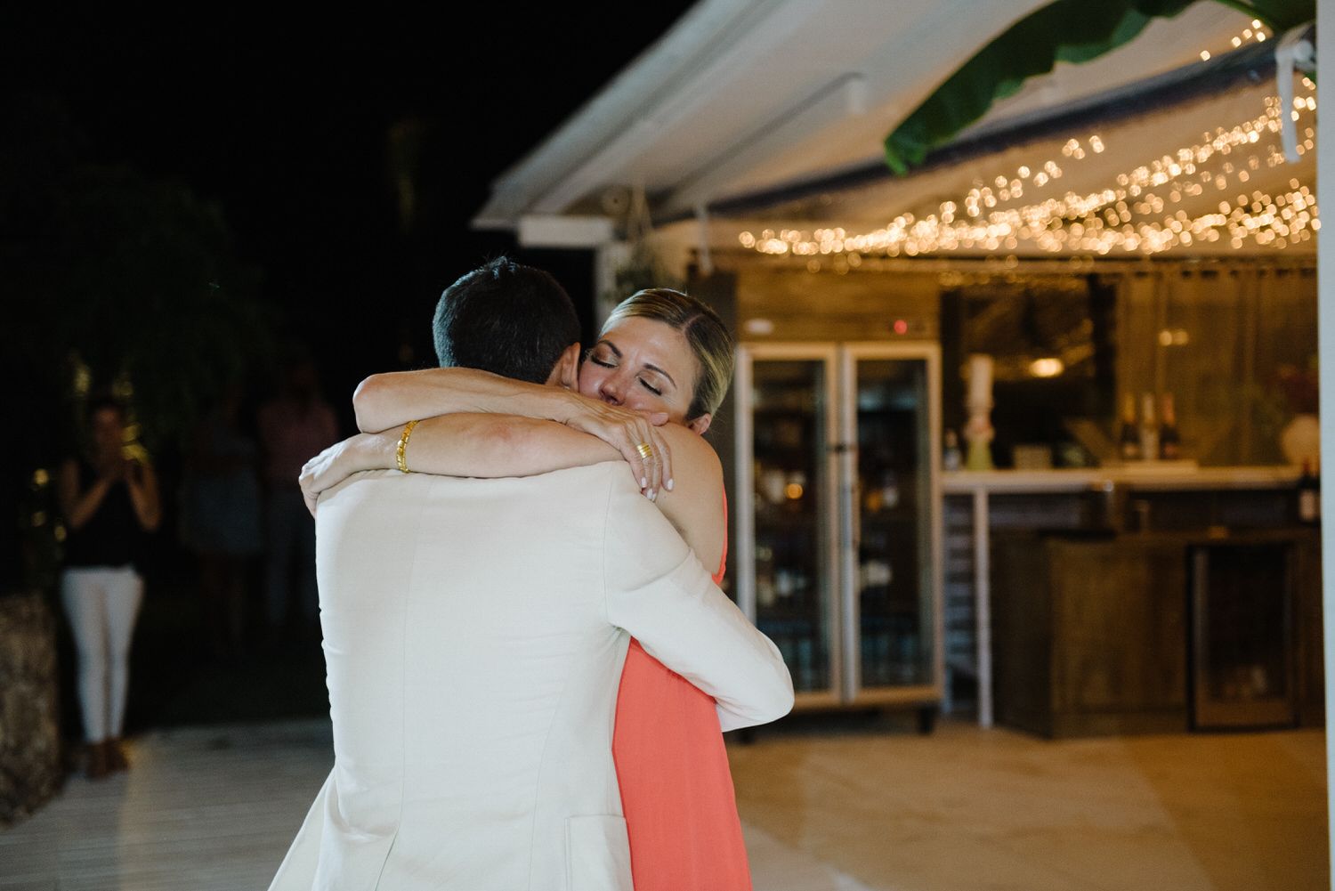 Heartfelt embrace shared during a wedding reception under glowing string lights.