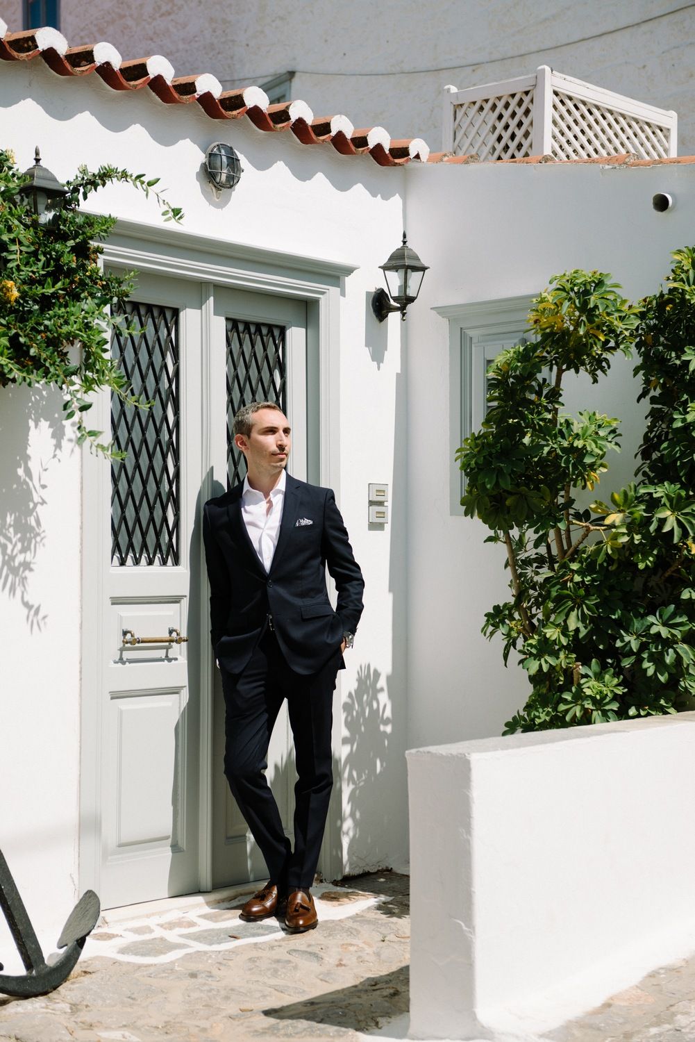 A person in a dark suit stands outside a Mediterranean-style white building with citrus trees.