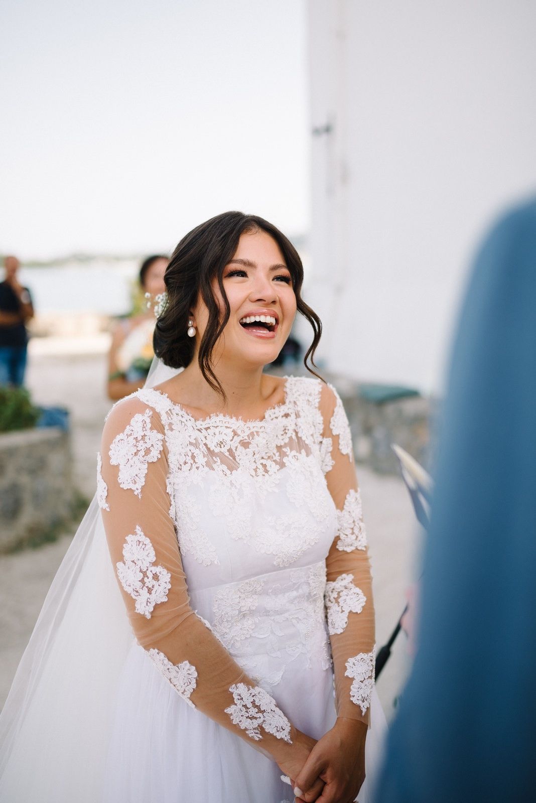 Bride in elegant lace sleeve wedding dress smiling joyfully outdoors.