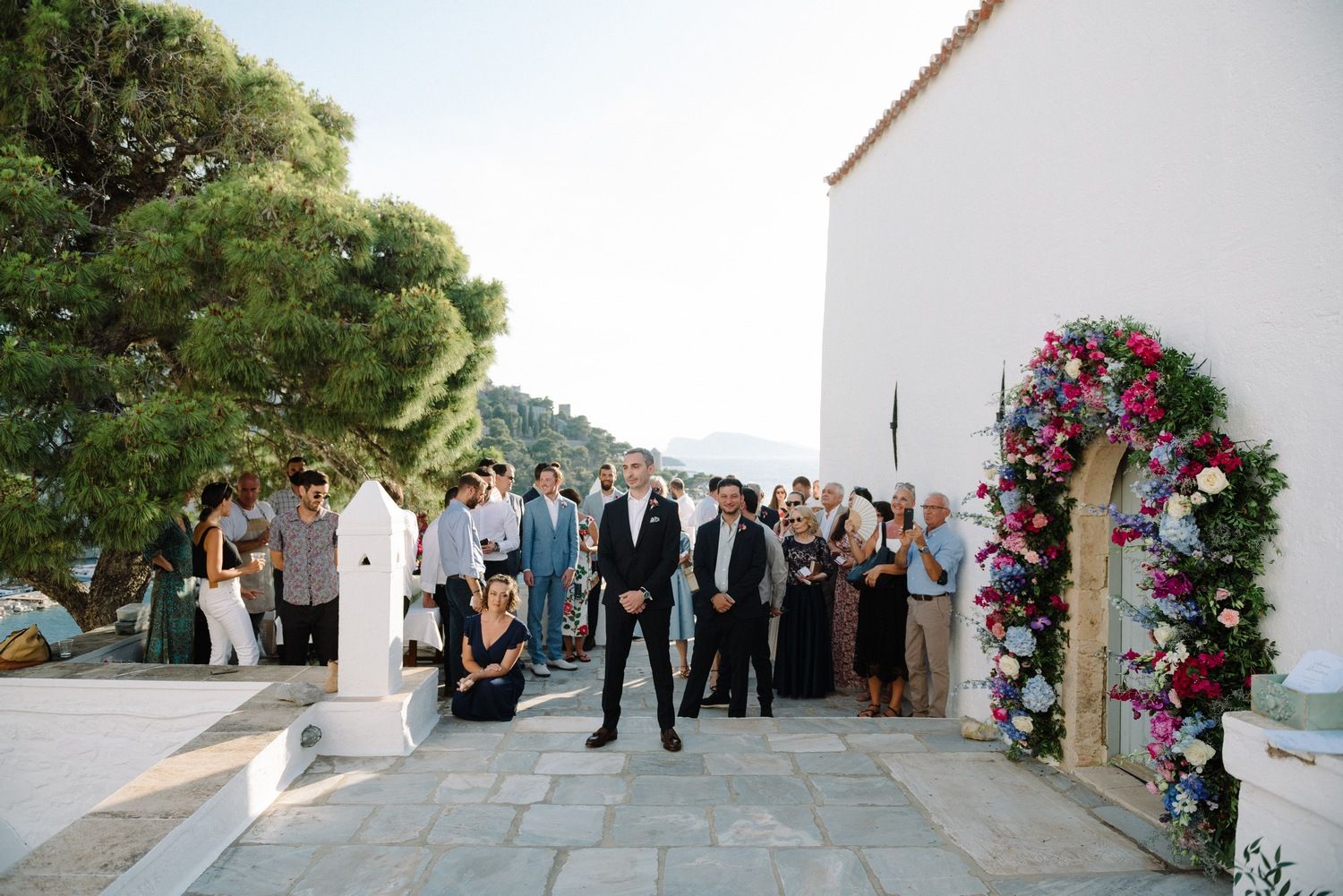 Wedding ceremony setup with floral arch and guests on Mediterranean terrace overlooking coastal scenery.