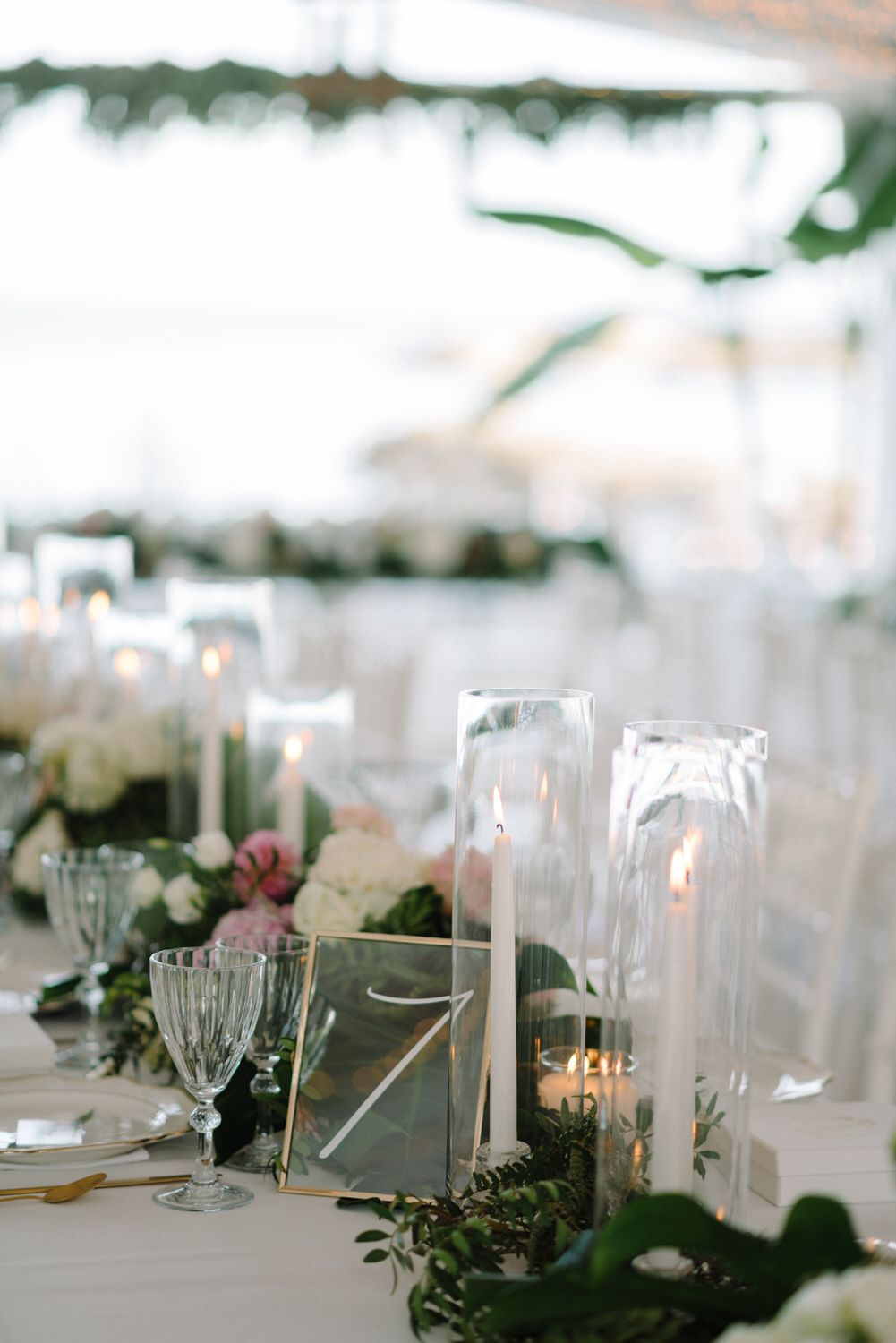 Elegant wedding table setting with glass hurricane candle holders and greenery garland decorations.