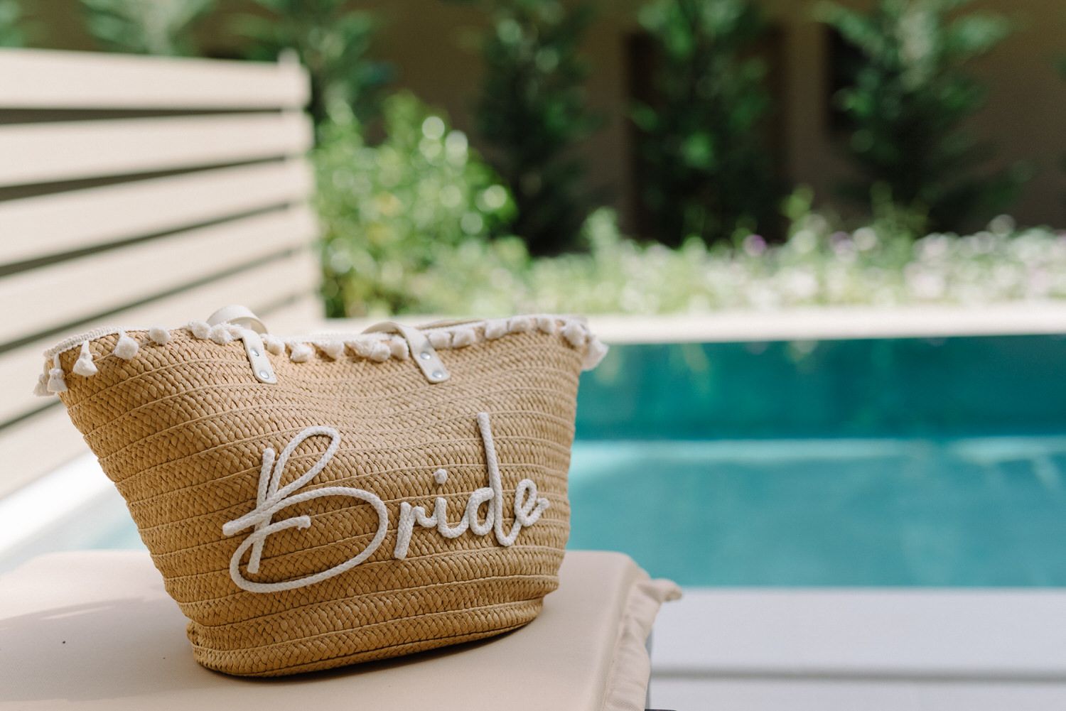 Straw beach bag with 'Bride' text next to swimming pool.