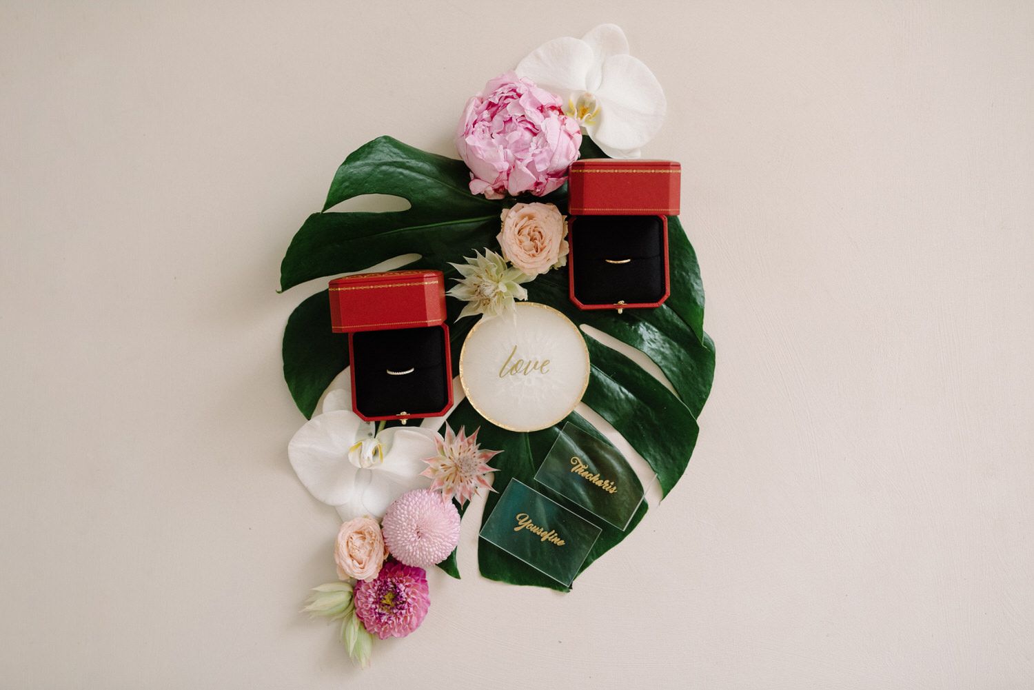 Wedding accessories and jewelry boxes arranged on monstera leaf with pink flowers.