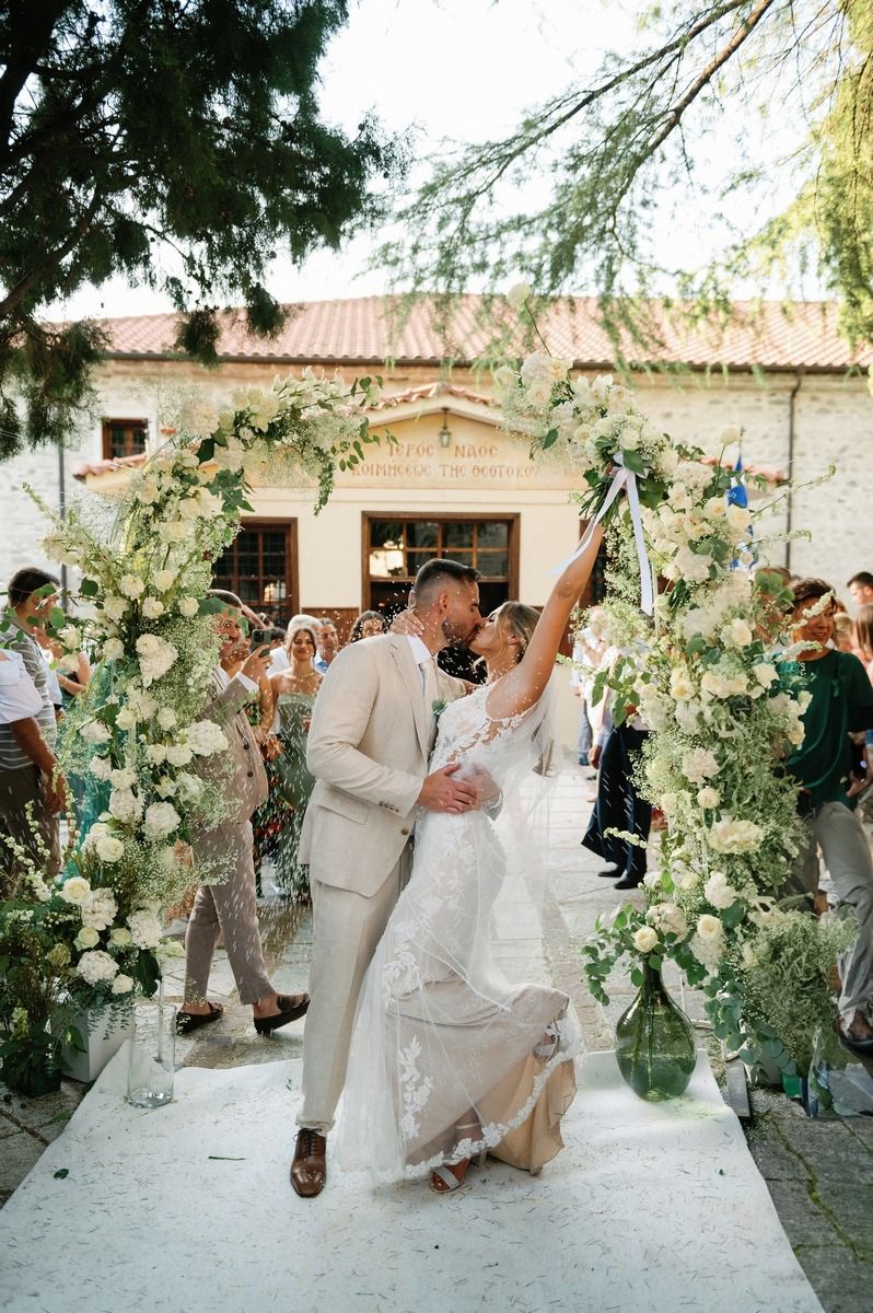 Romantic celebration under floral arch with white roses and greenery.