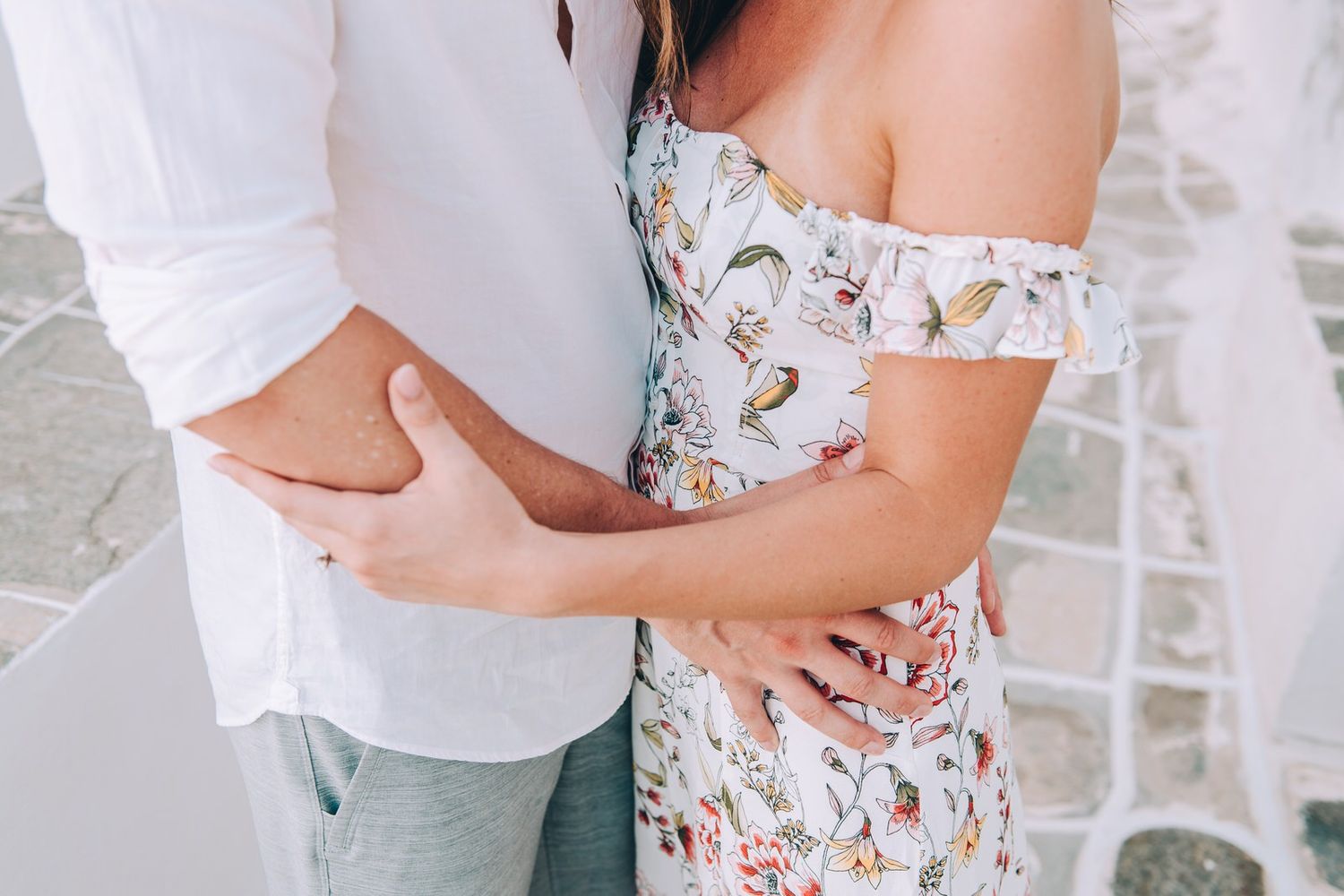 Close-up of embracing couple wearing white and floral patterns against Mediterranean architecture.