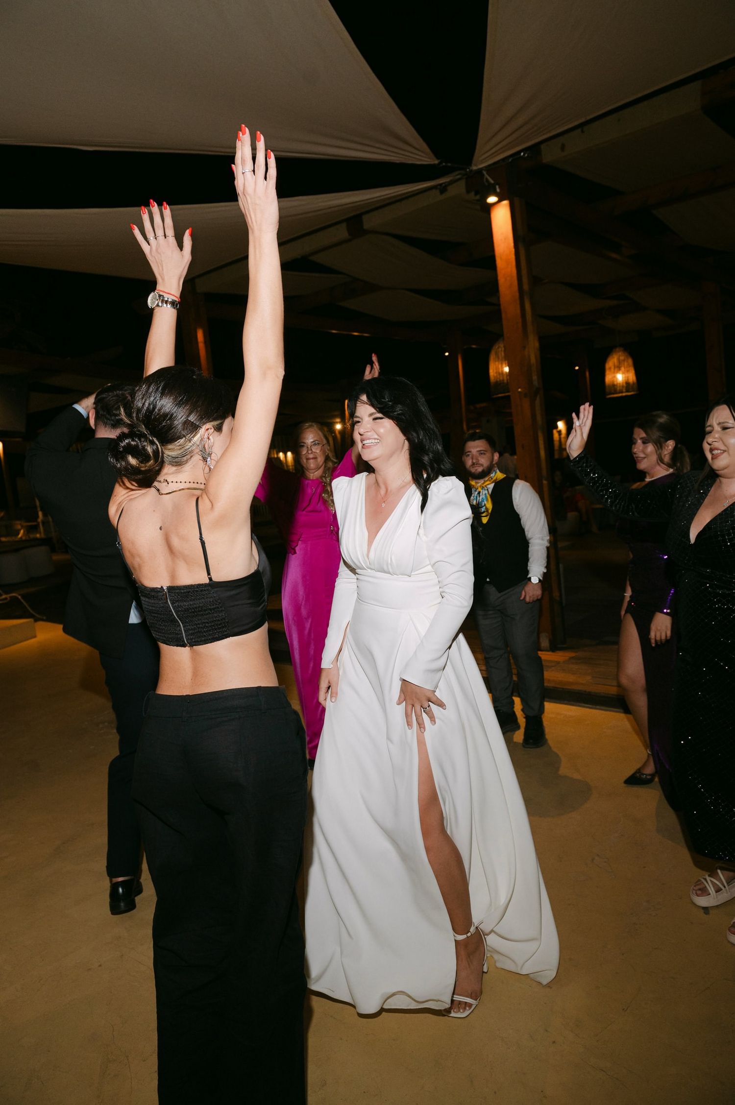 Two people dancing energetically at a wedding reception, one in a white dress and one in black attire.