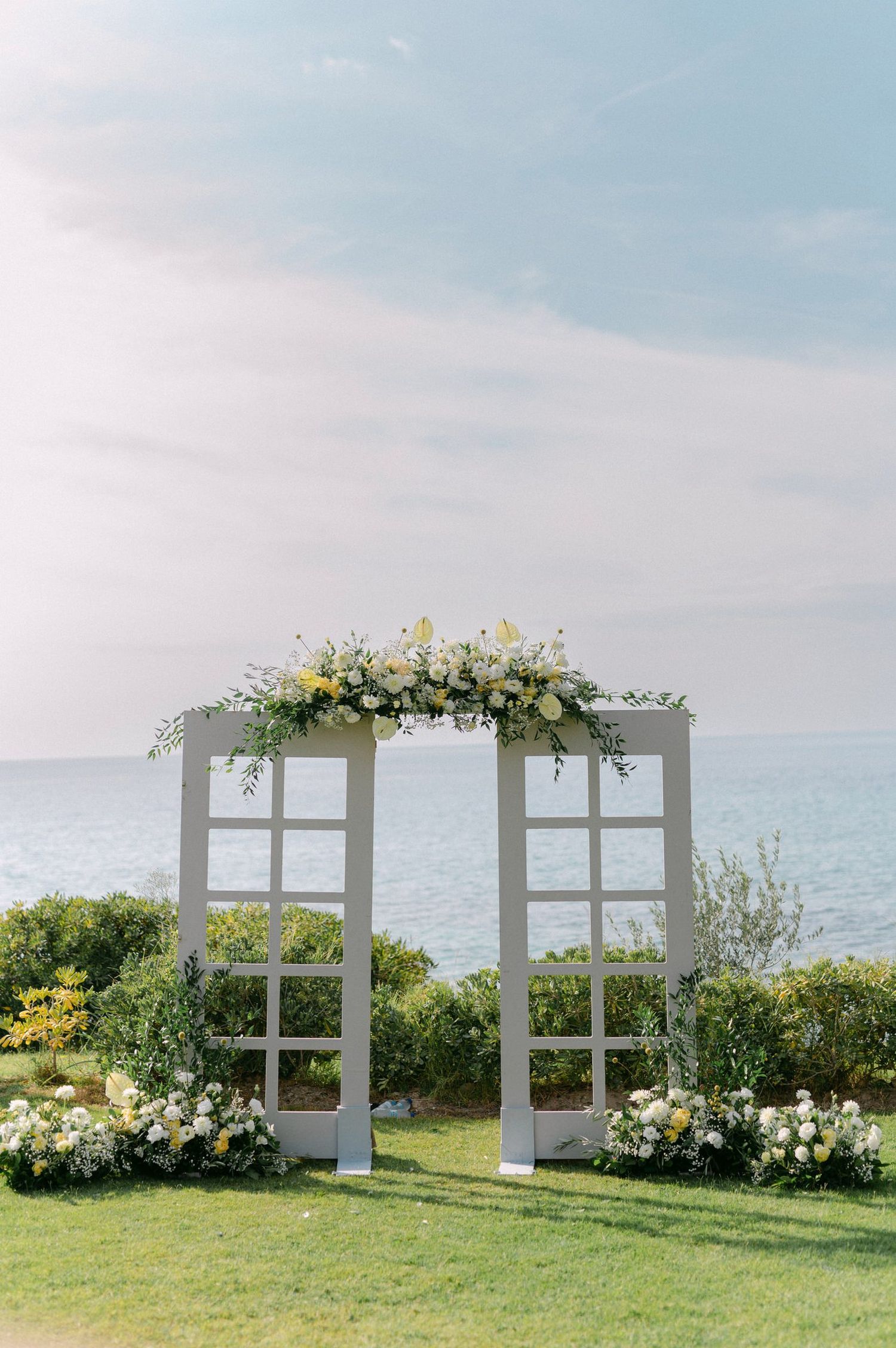 White decorative window frames create a romantic seaside wedding backdrop with yellow and white floral arrangements.