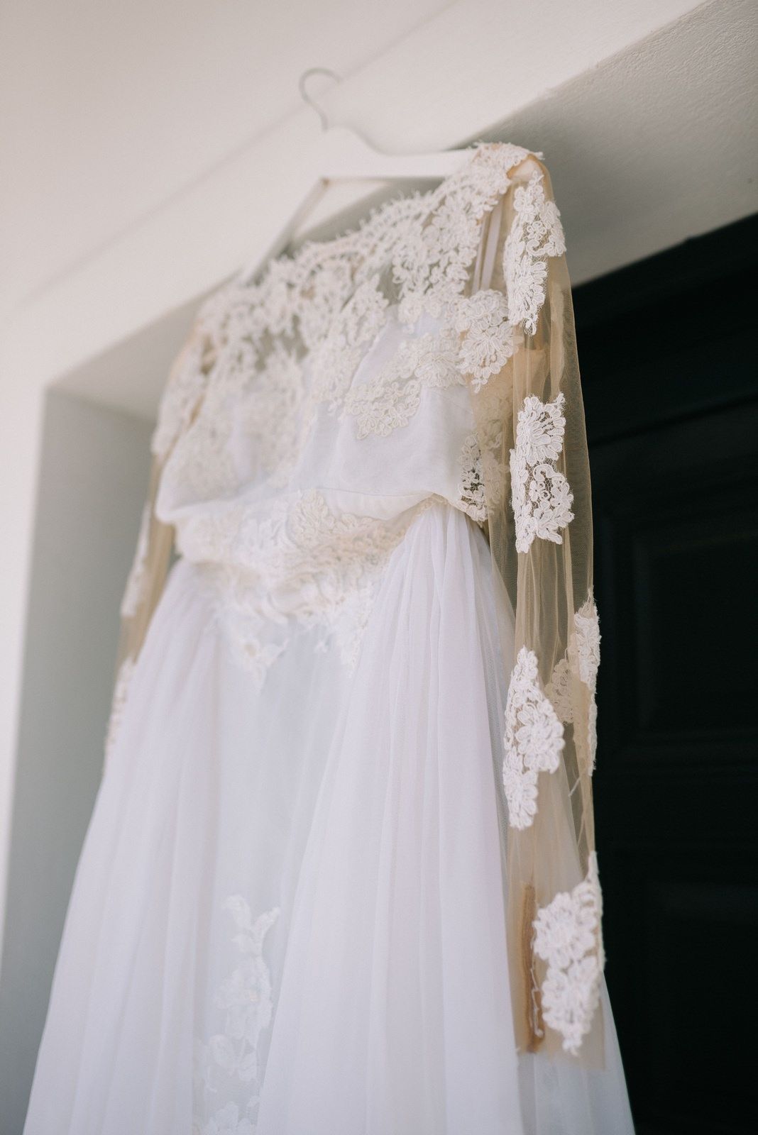 A delicate white lace wedding dress with flowing tulle skirt hanging on display.