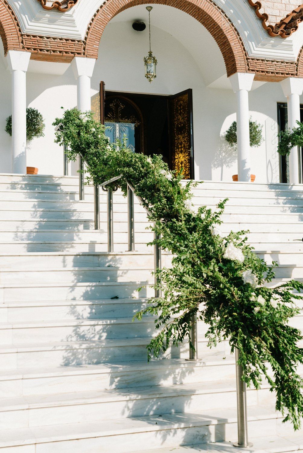 White stone steps leading to an arched entrance with greenery decorations along the railing.