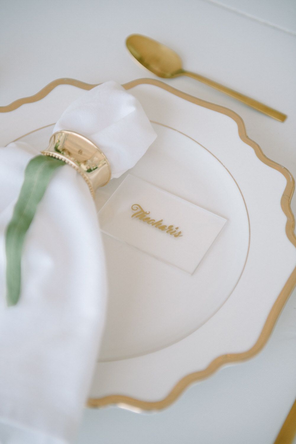 Close-up of luxurious white and gold place setting with name card and napkin ring.