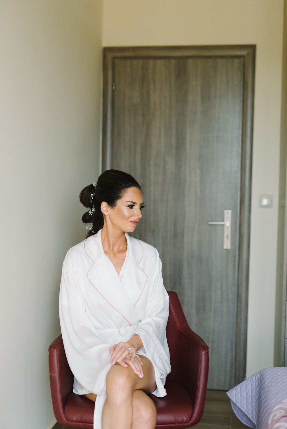Person in white robe sitting in burgundy chair during wedding preparations.