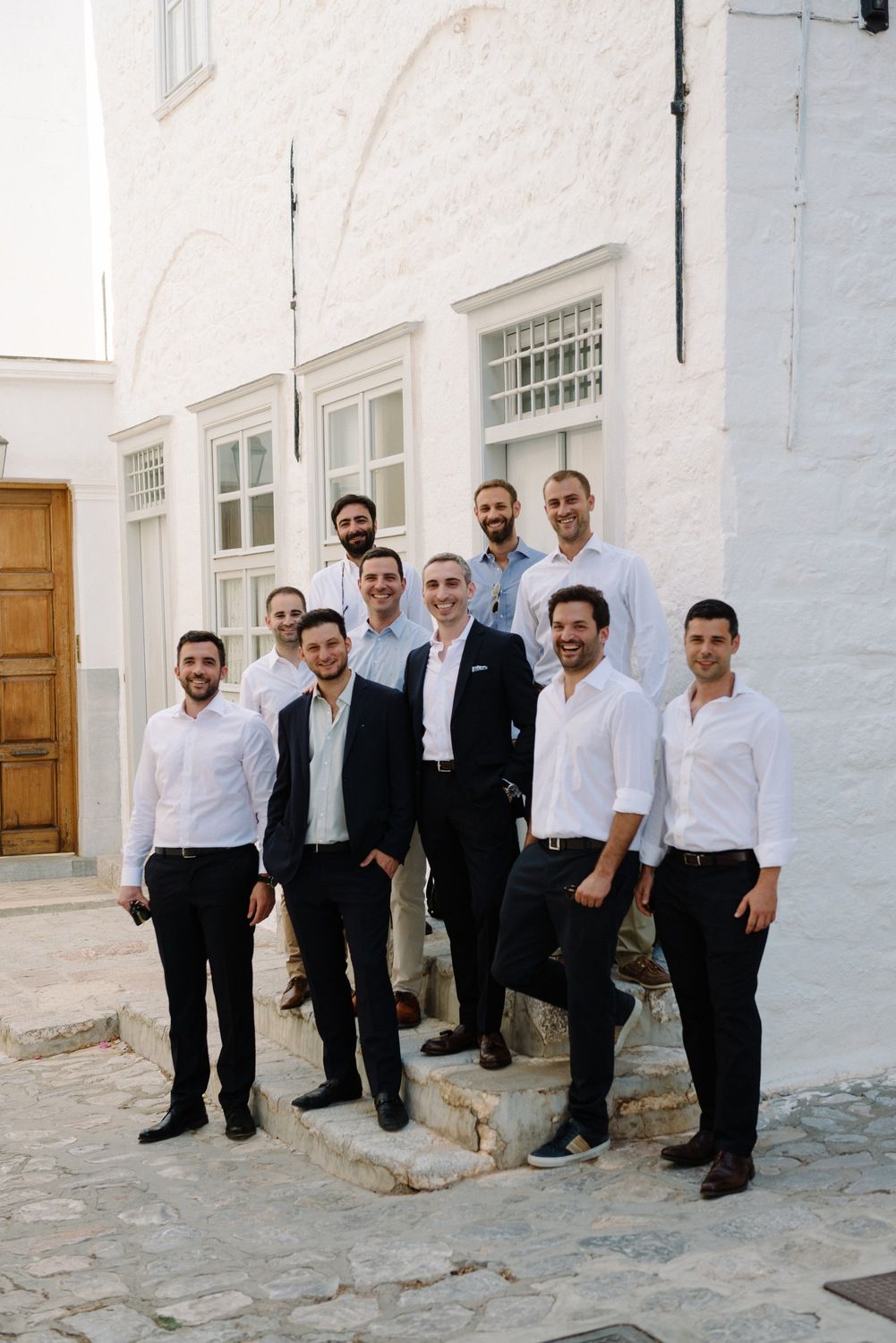 A group of people in formal attire pose on white stone steps.