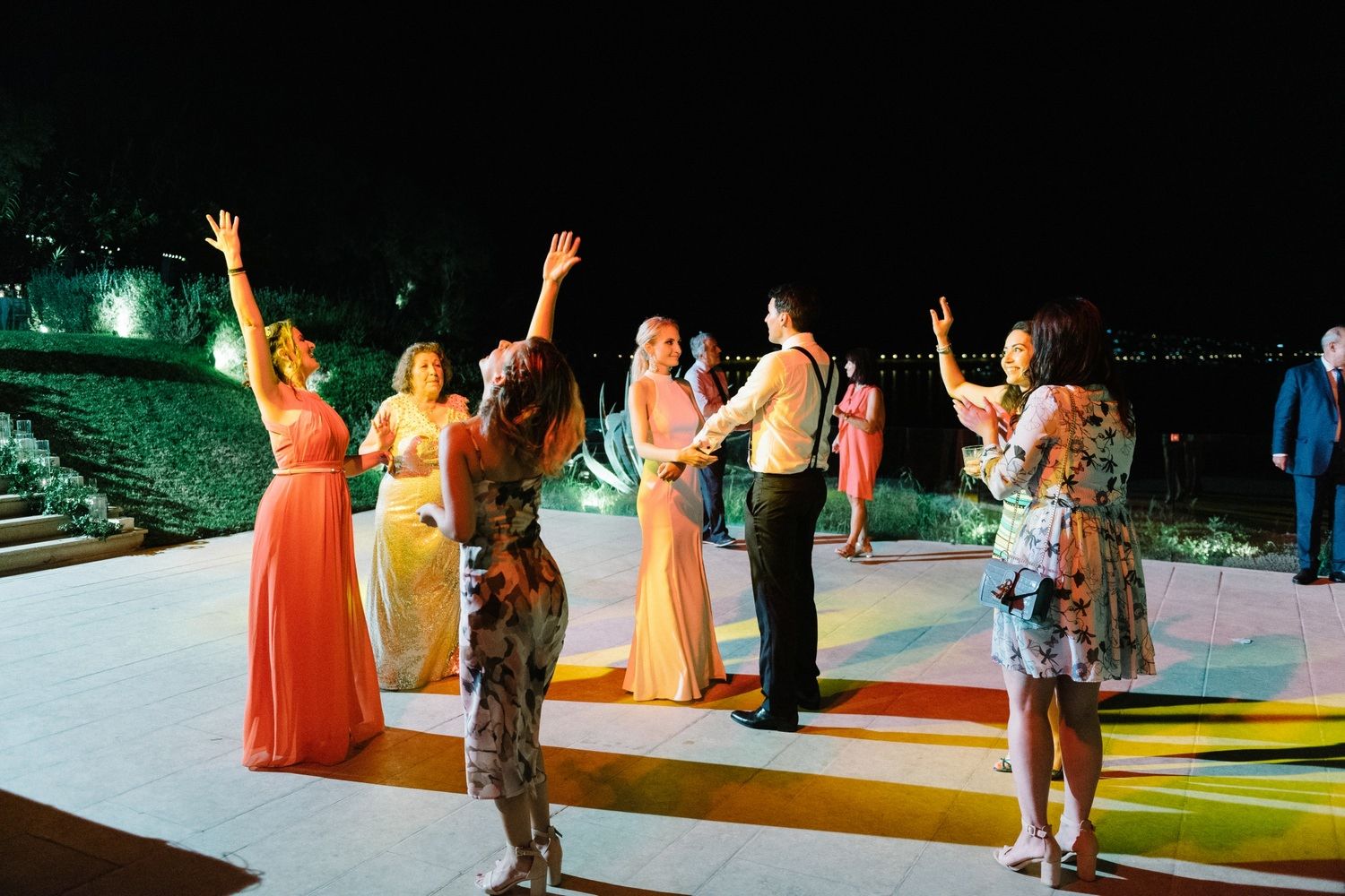 Wedding guests dancing and celebrating on a colorfully lit outdoor dance floor at night.