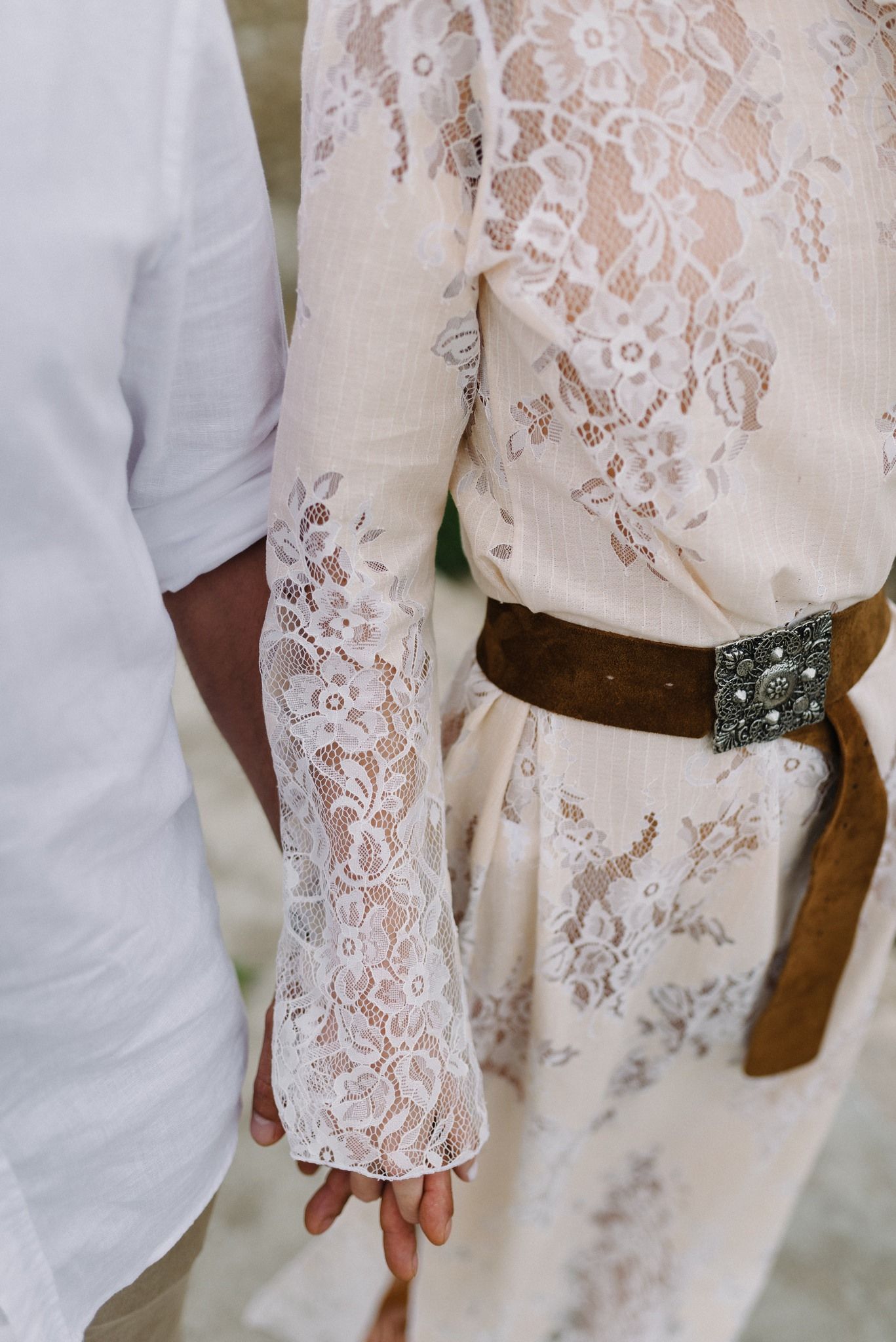 Detail shot of lace sleeve and brown leather belt with ornate buckle.