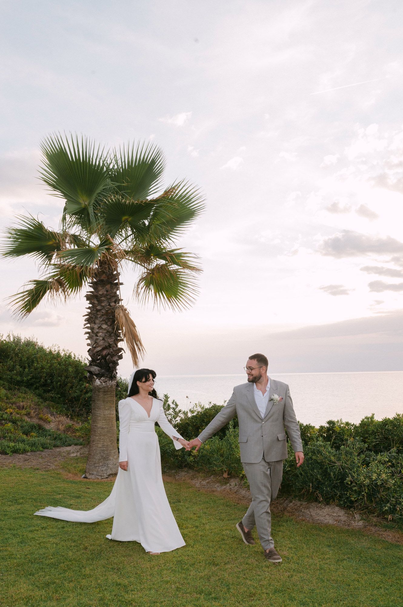 Couple walking and posing playfully near palm trees at sunset during a beach wedding photoshoot in Halkidiki Greece.