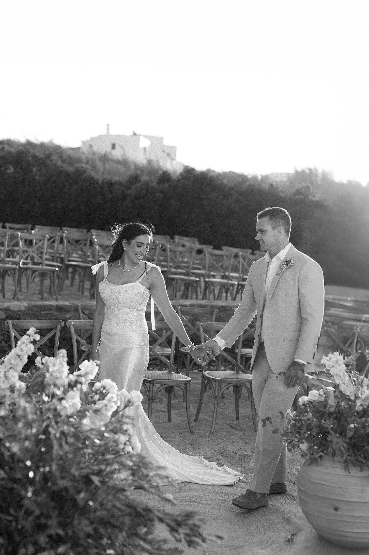 A couple in wedding attire poses for romantic black and white photos in a garden setting at sunset in Mykonos Greece