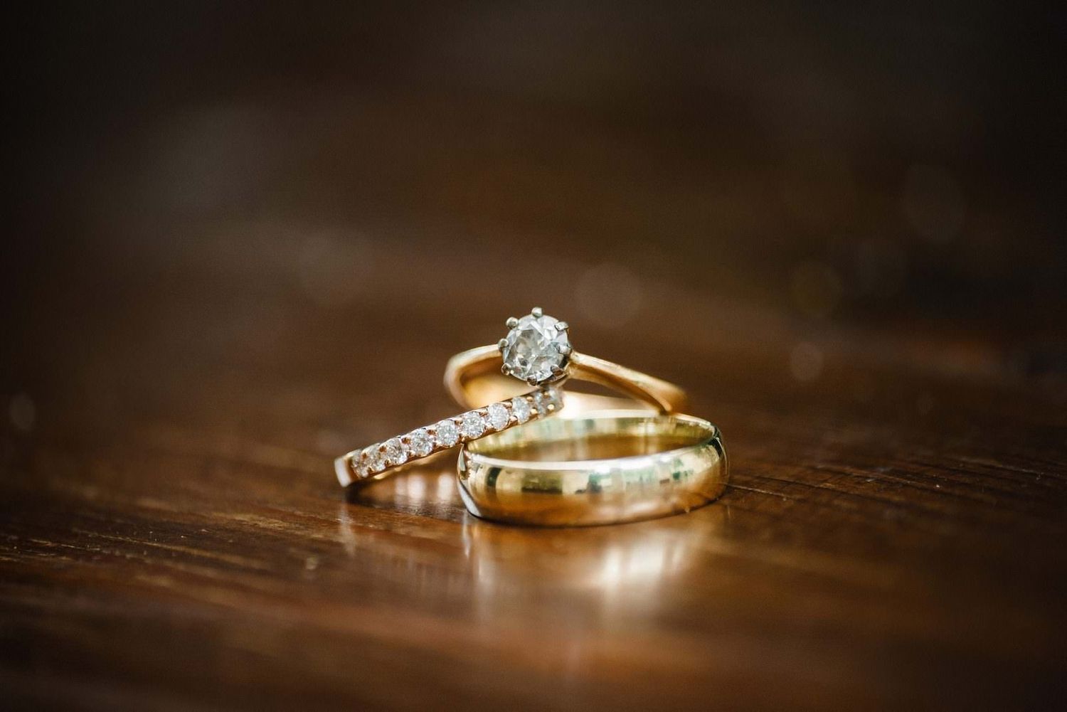 Wedding rings featuring diamond engagement ring and gold band photographed on wooden surface.
