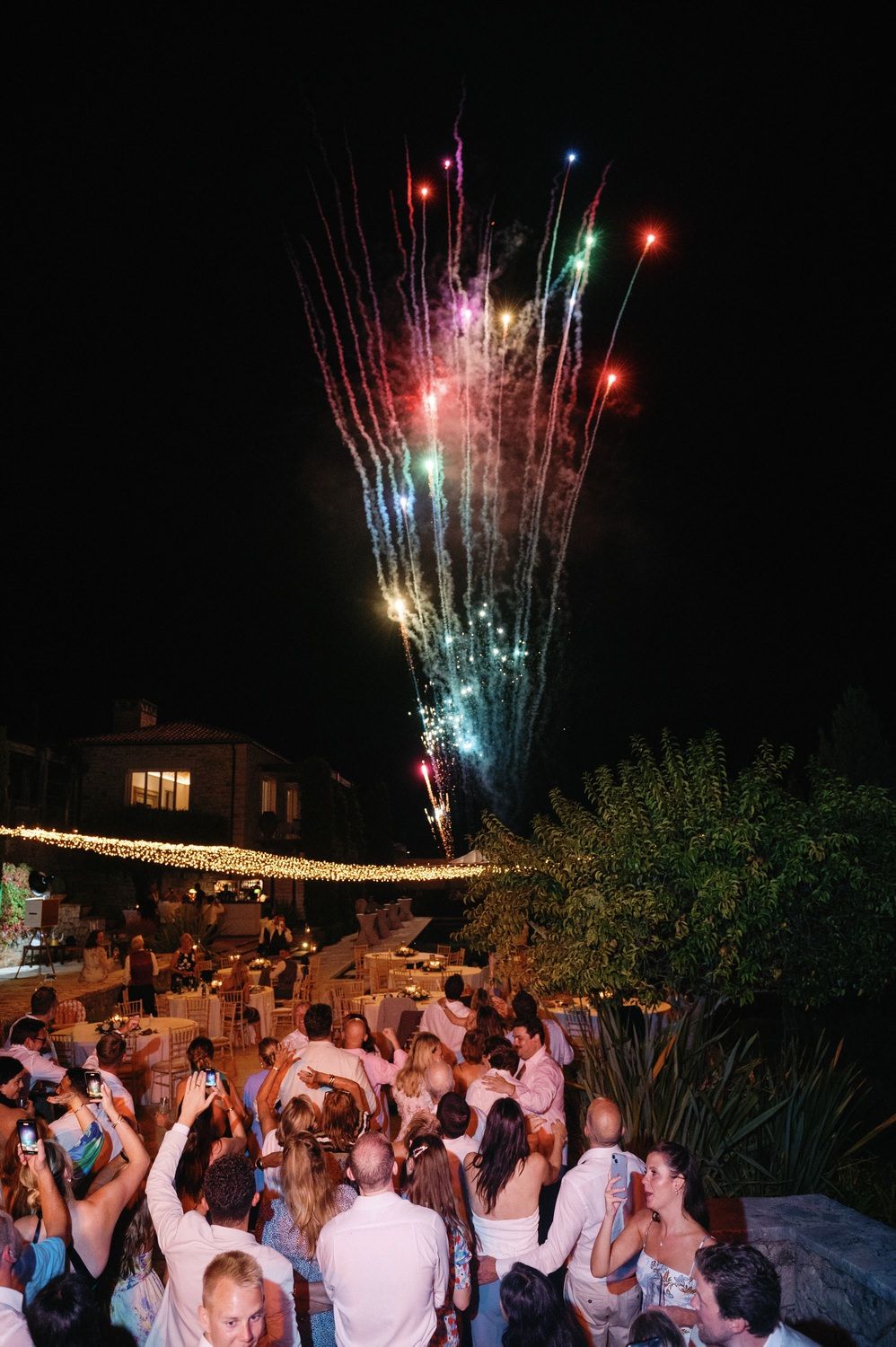 Colorful fireworks display bursting over crowd at outdoor nighttime celebration.