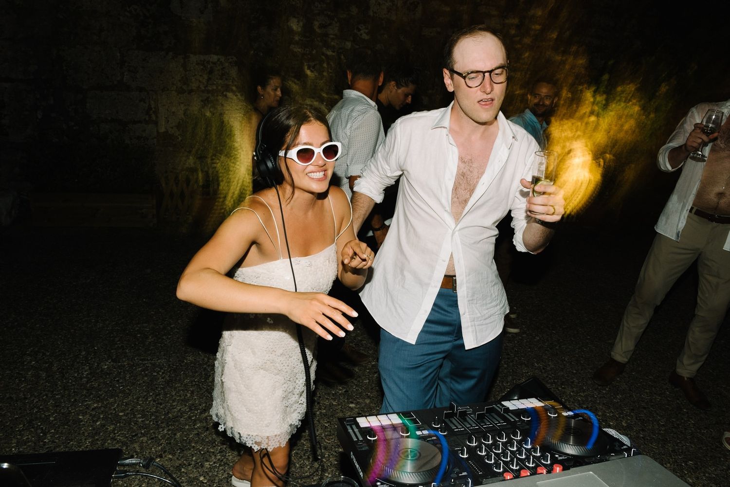 Wedding guests dance near DJ equipment at a nighttime celebration.