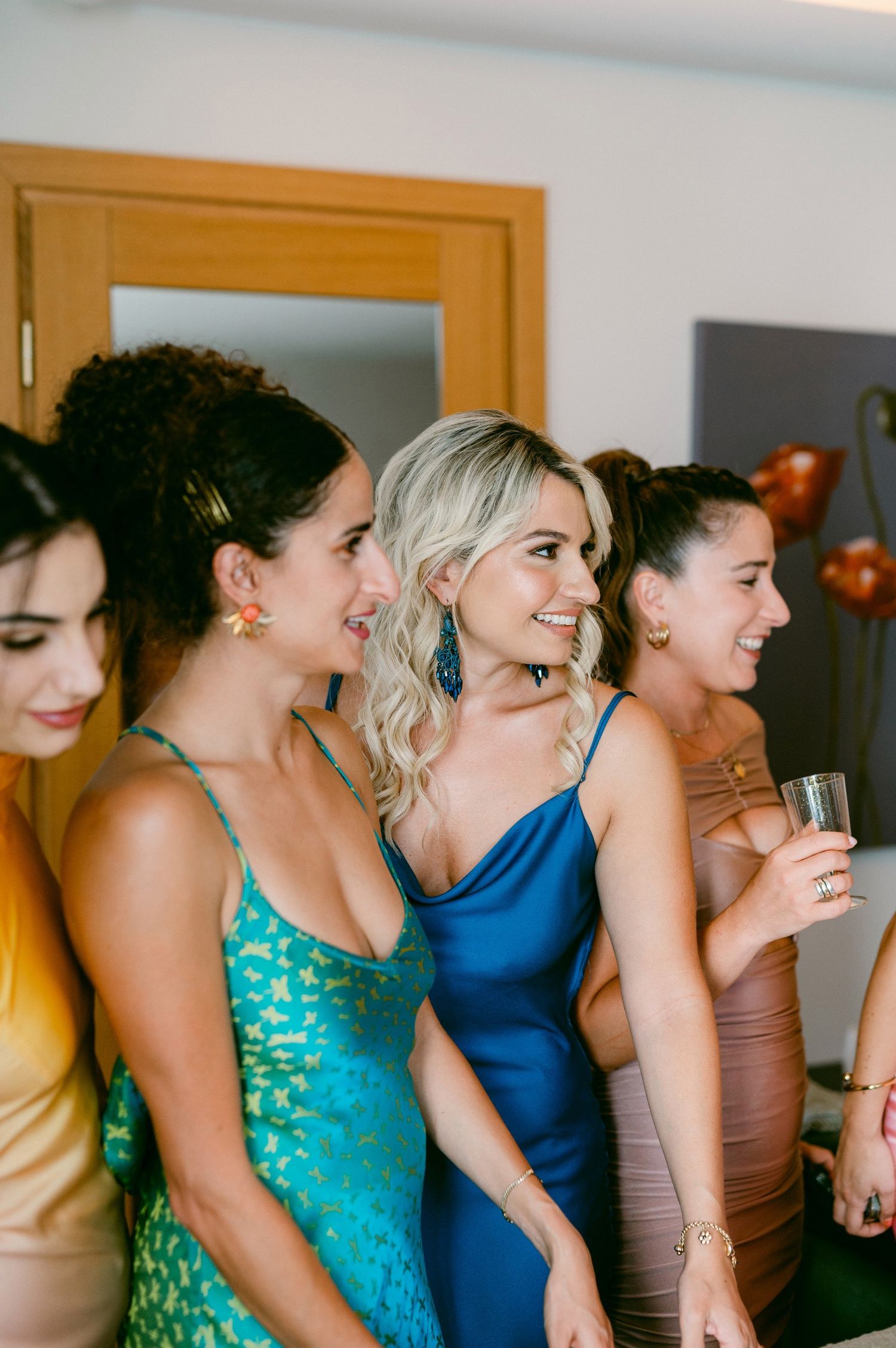 Group of friends in formal event dresses, wearing turquoise, blue and tan colors, enjoying drinks at a celebration.