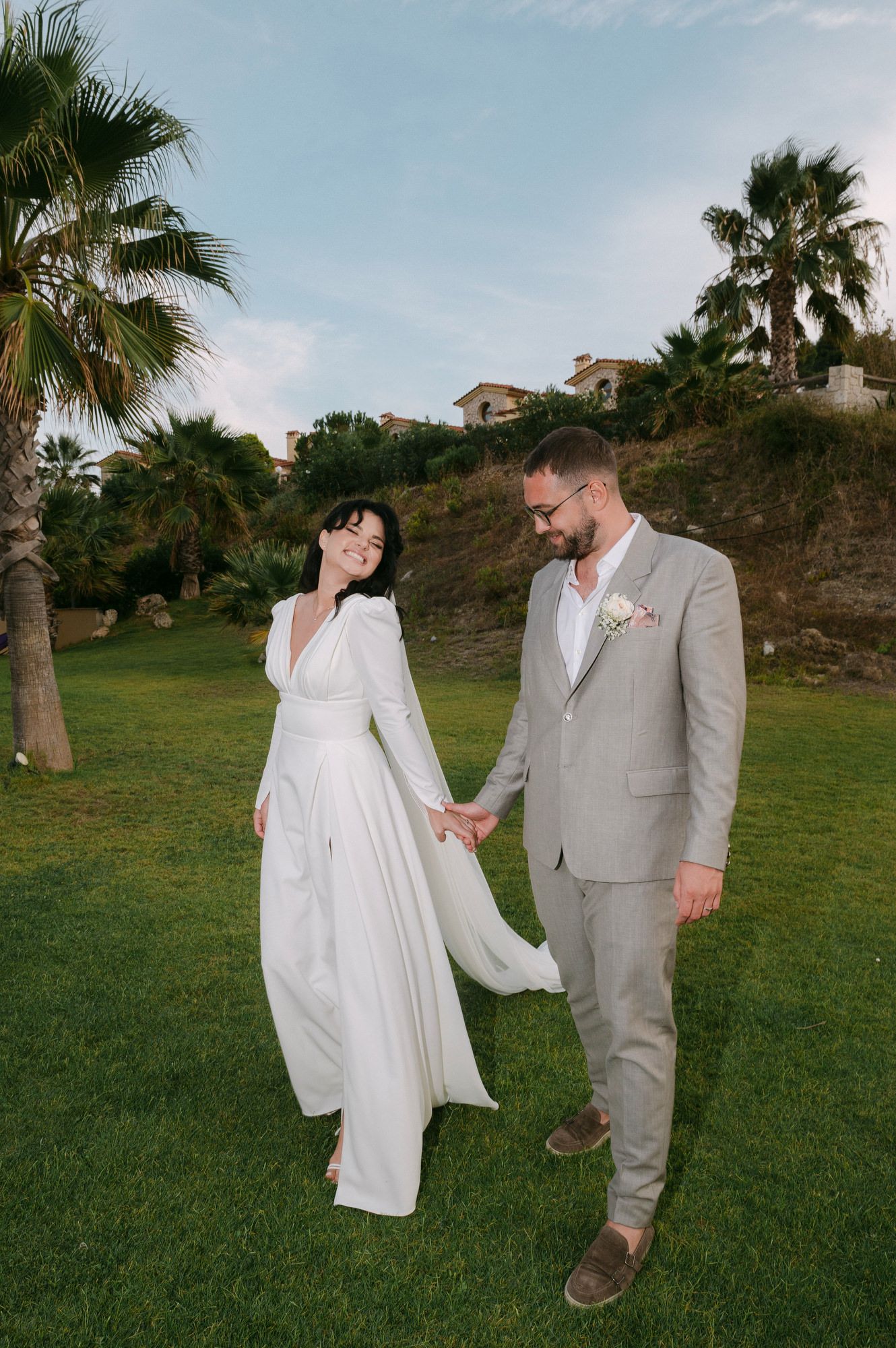 A couple walking together on a grassy hillside overlooking the ocean during golden hour.