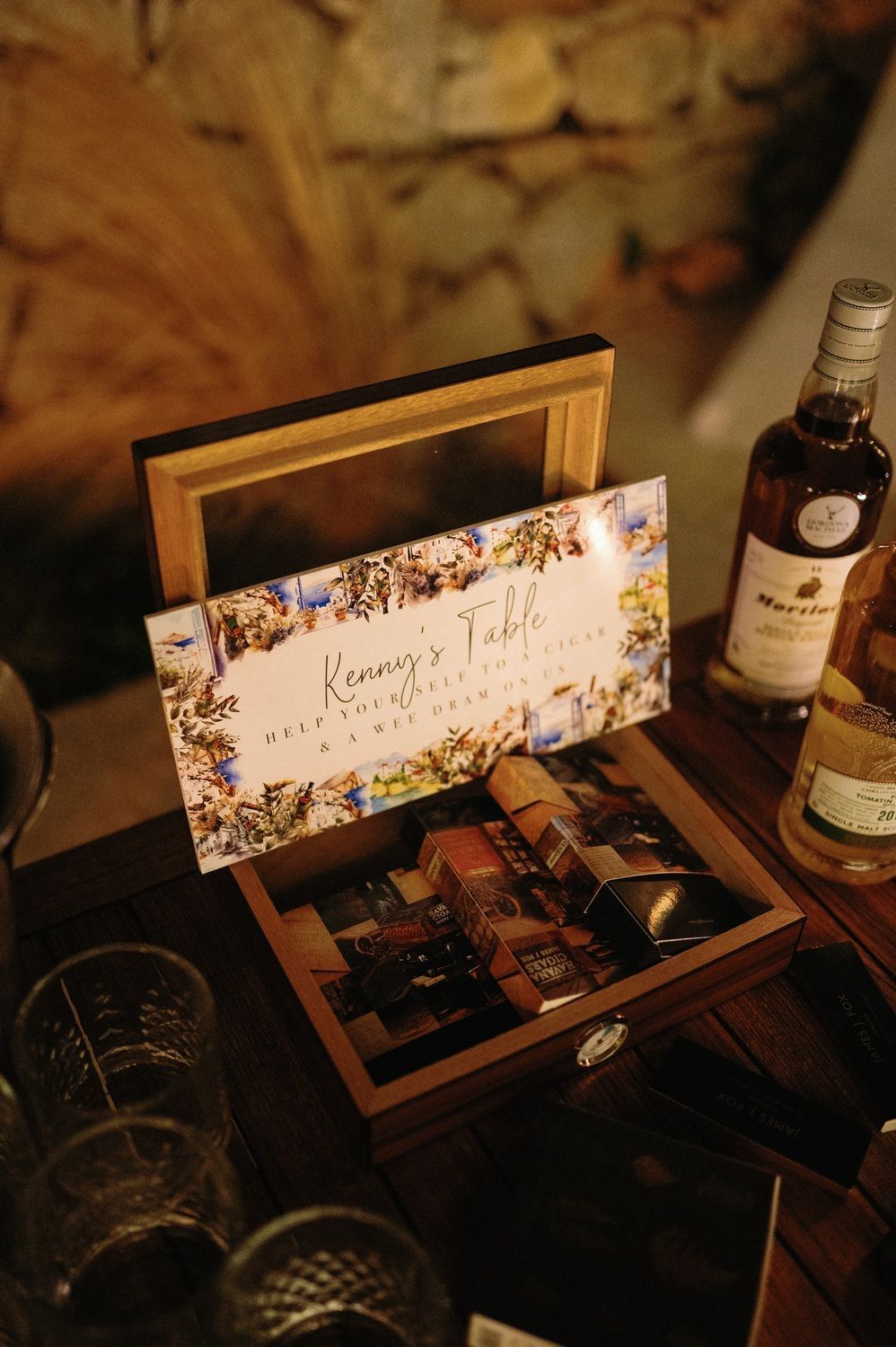 Wedding table place cards and bottles arranged on a dark wooden surface in moody lighting.
