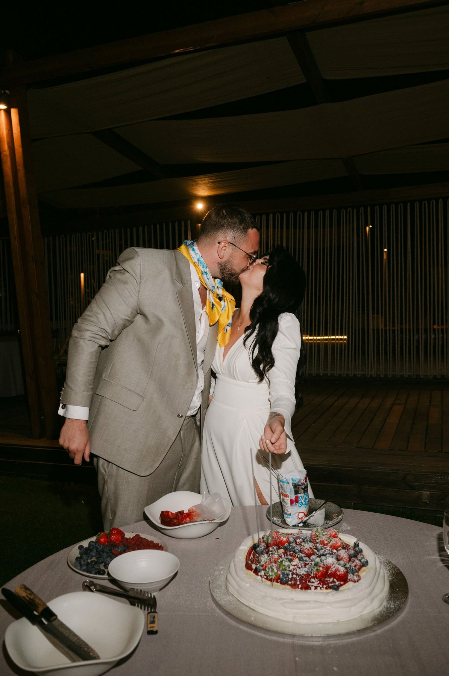 A couple cuts their wedding cake together in a dimly lit reception venue.