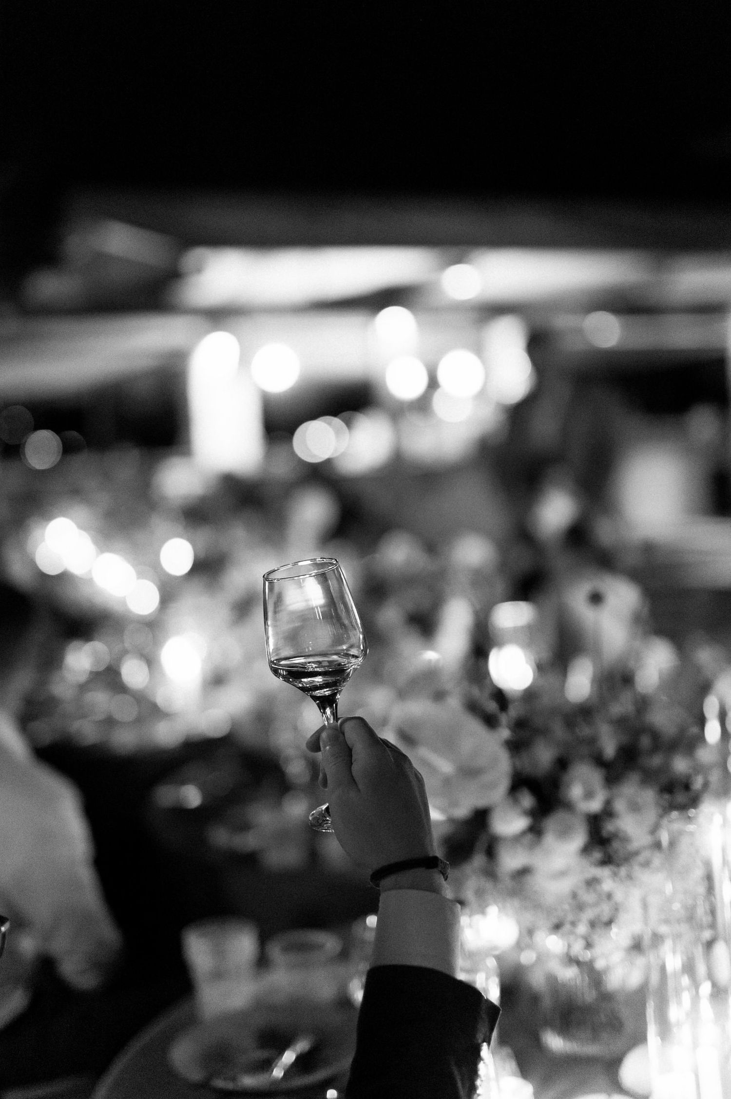 Black and white image of wine glasses on tables with soft bokeh lights creating an elegant atmosphere.