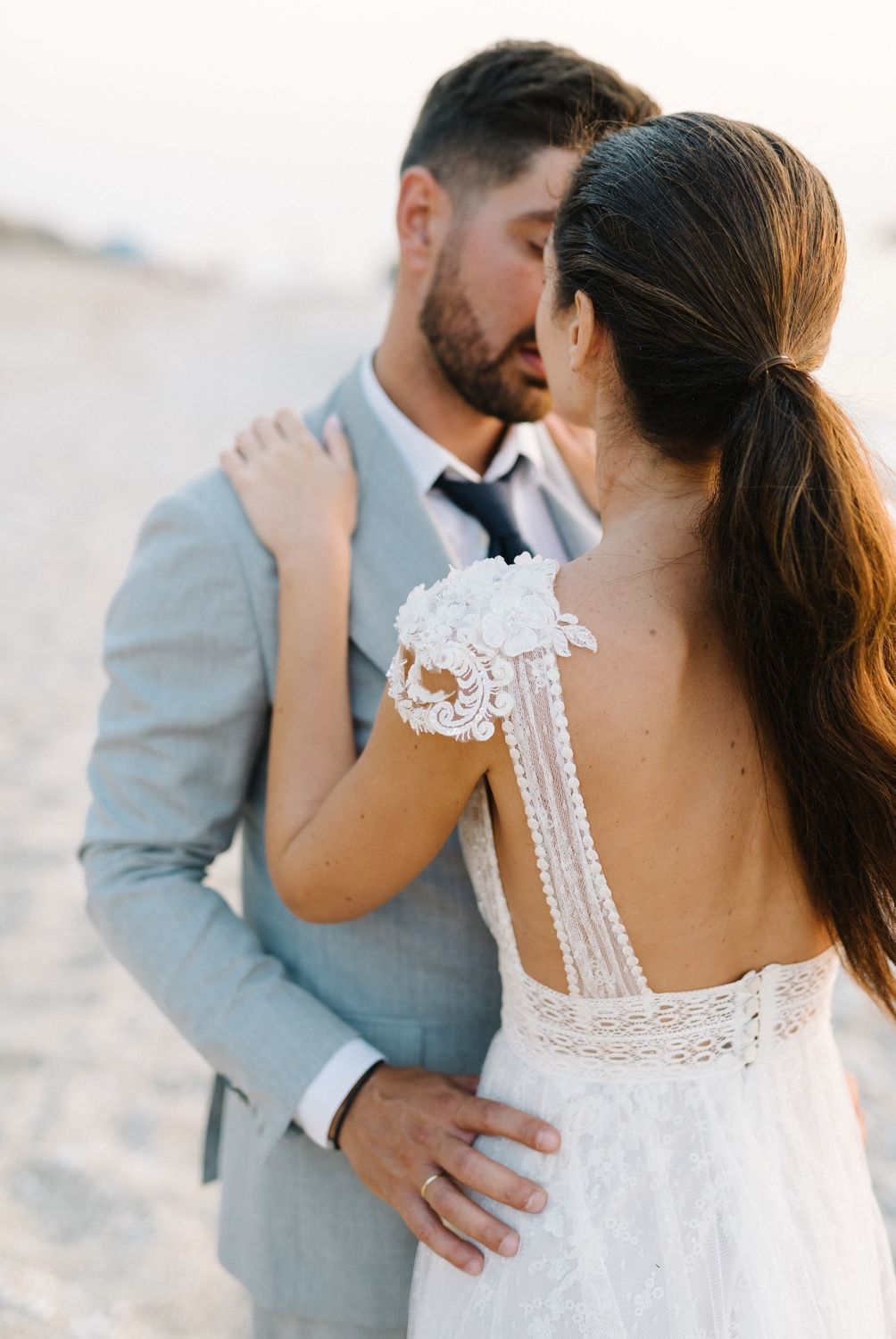 An intimate wedding portrait showcases the detailed lace back of a white bridal gown against a grey suit.