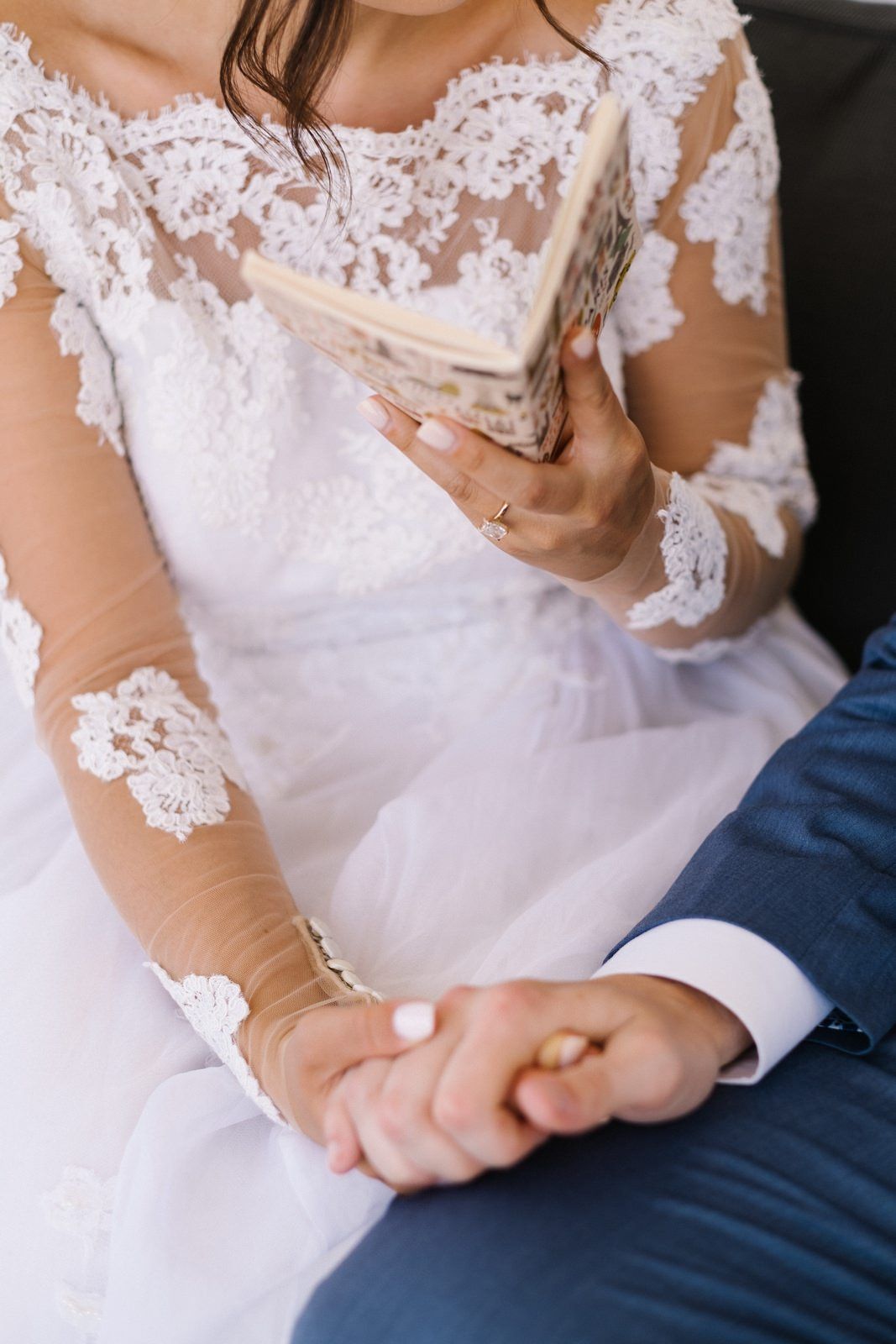 Close-up of bridal hands holding vintage book with lace dress details.