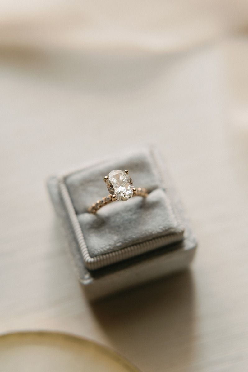 A delicate diamond engagement ring nestled in a grey velvet ring box photographed from above.