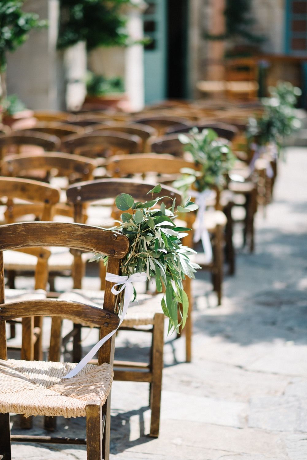 Wooden chairs decorated with greenery arranged for an outdoor wedding ceremony.