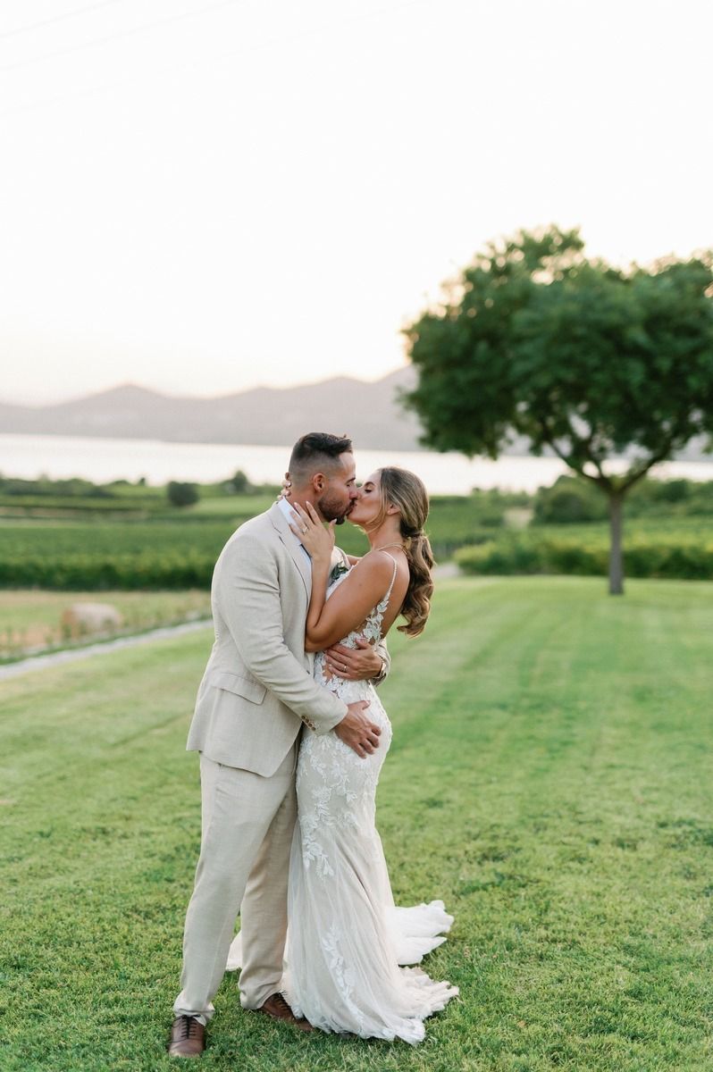 Romantic wedding couple embracing on hillside with mountain and lake views.