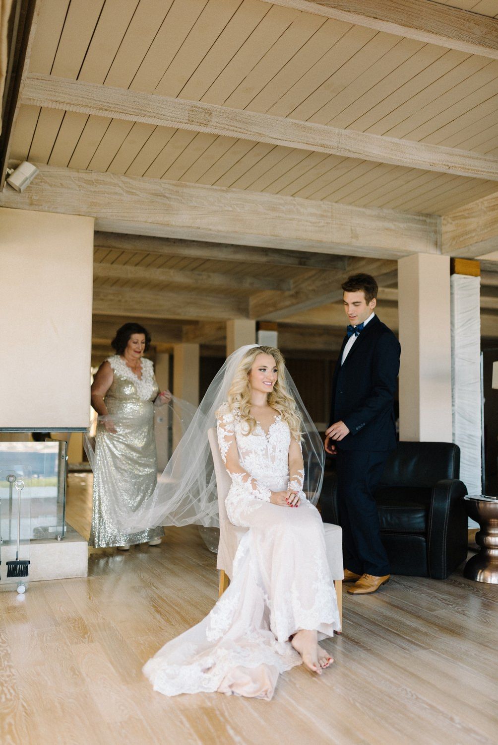 Wedding scene with elegant bride in lace gown seated while others look on.