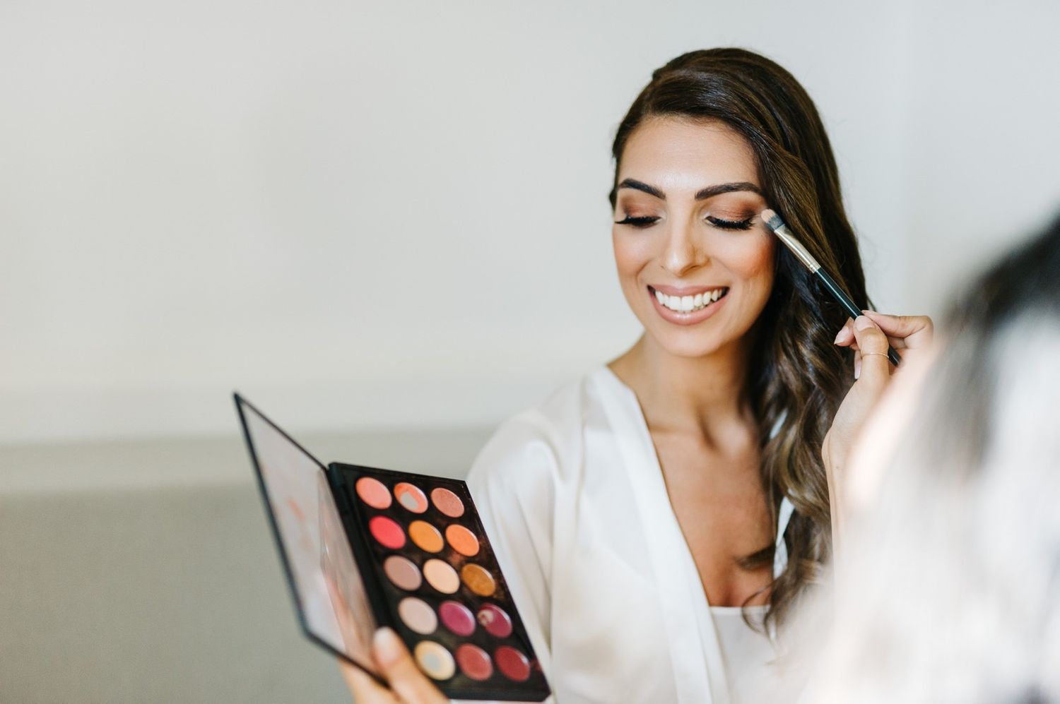 Professional makeup session with eyeshadow palette and brushes in soft lighting.