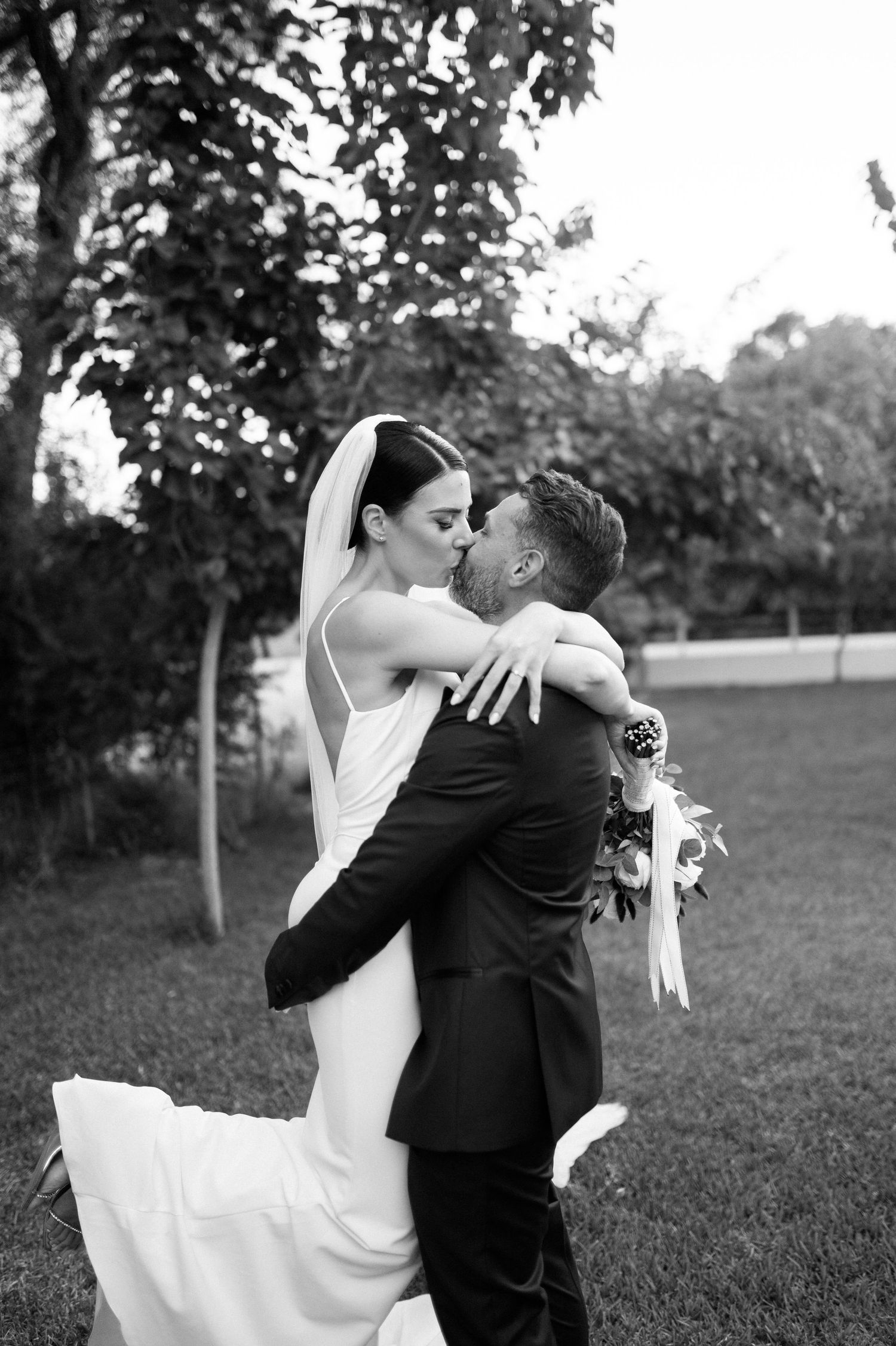 A couple in wedding attire dances together in a romantic pose on a grassy lawn.