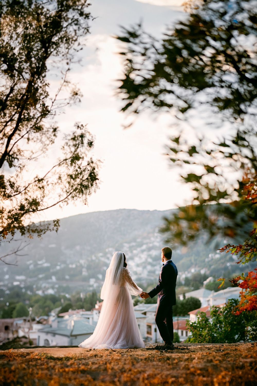 Silhouetted couple stands on a scenic overlook with mountains and water in the background during sunset.