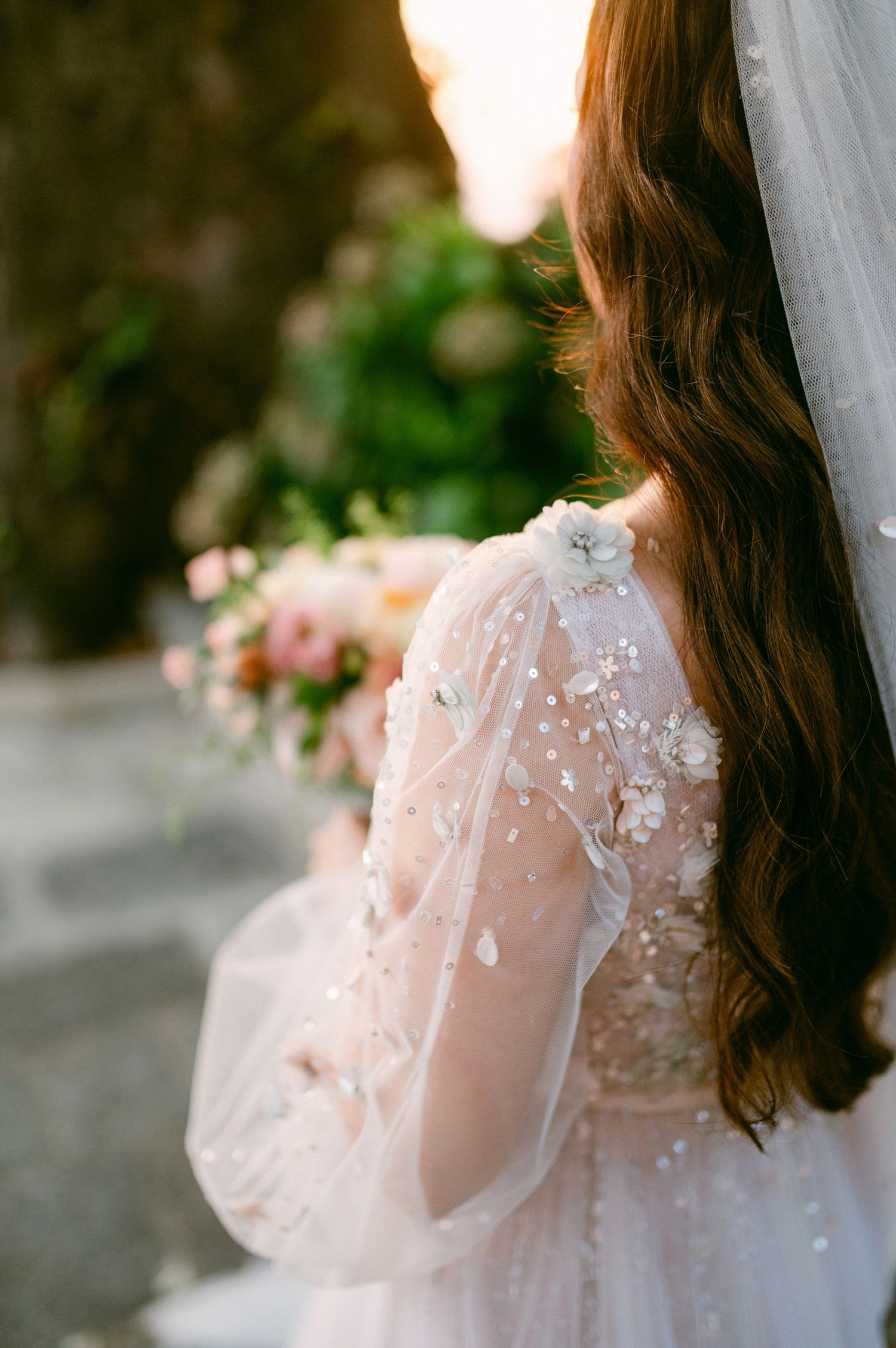Close-up detail of intricate lace and beading on a white wedding gown with flowing veil and bouquet.