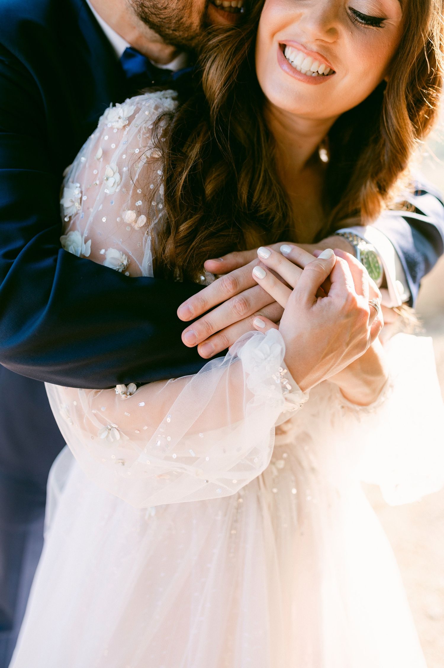 Intimate wedding moment showing couple embracing with bride wearing delicate beaded white gown and sheer sleeves.