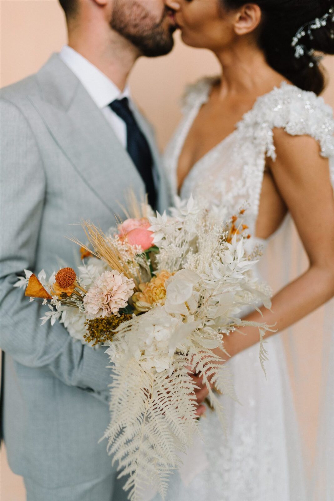 A romantic wedding couple shares a tender kiss while holding a delicate bouquet of dried flowers and pampas grass.