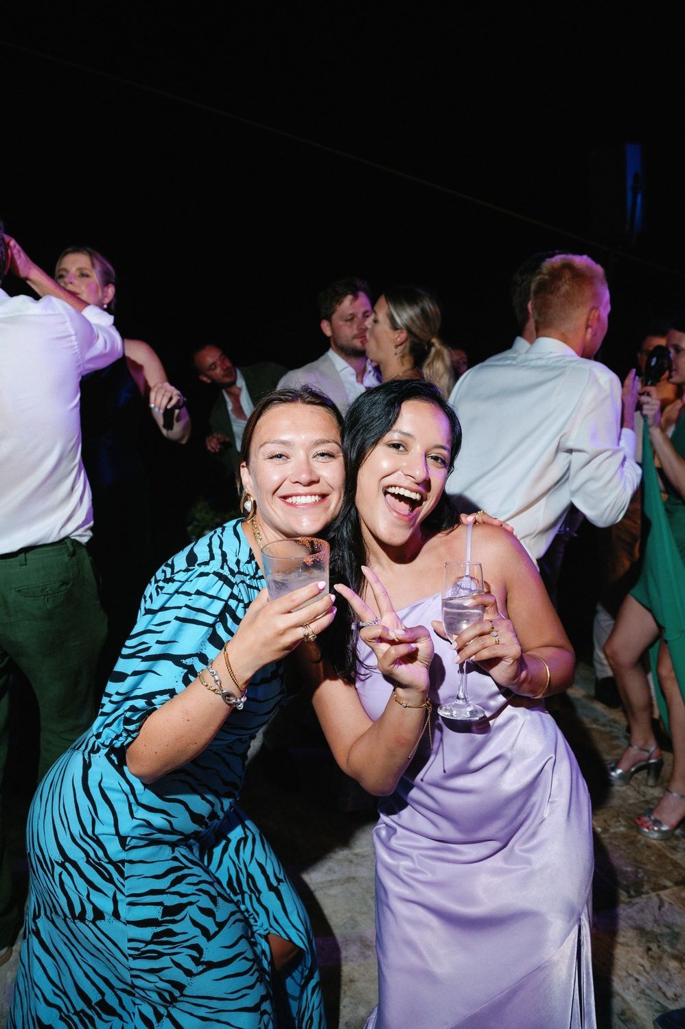 Two people dancing together and laughing at a party with one wearing a turquoise striped top and another in purple.