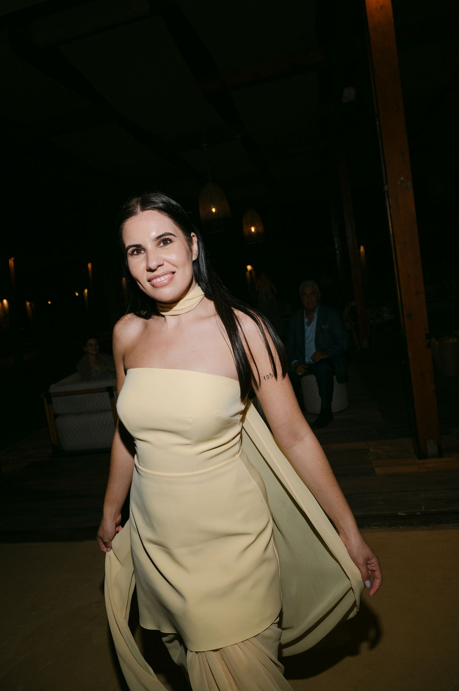 A woman in a cream-colored strapless dress smiles while standing outdoors at night.