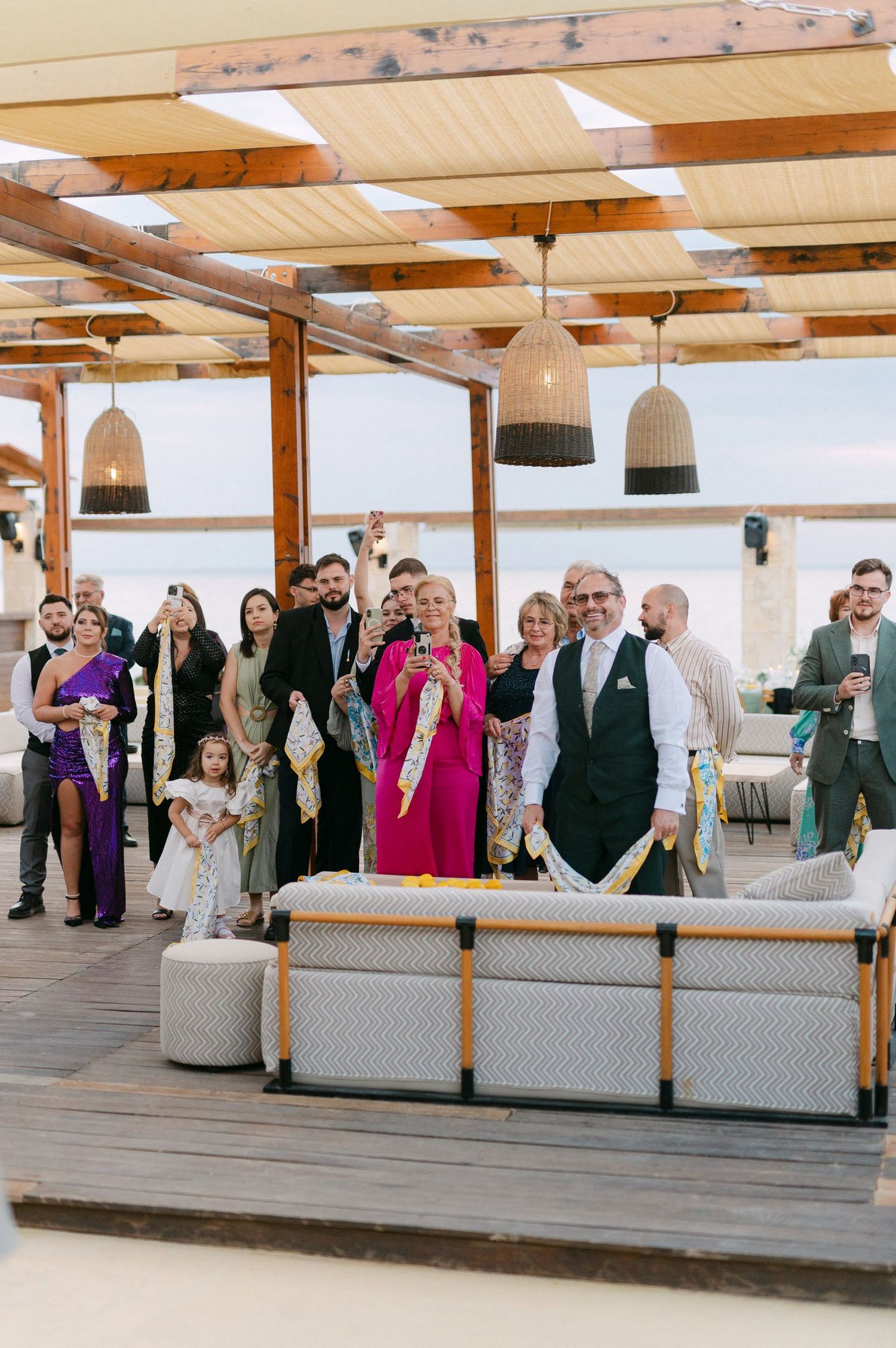 Wedding guests seated on white benches in a rustic indoor venue with wooden beams and pendant lighting.