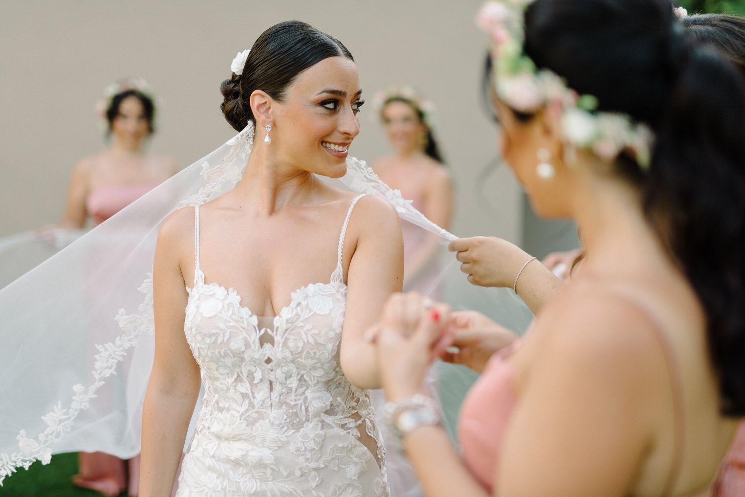 Candid moment of wedding preparation with bridesmaids adjusting the bride's veil outdoors.