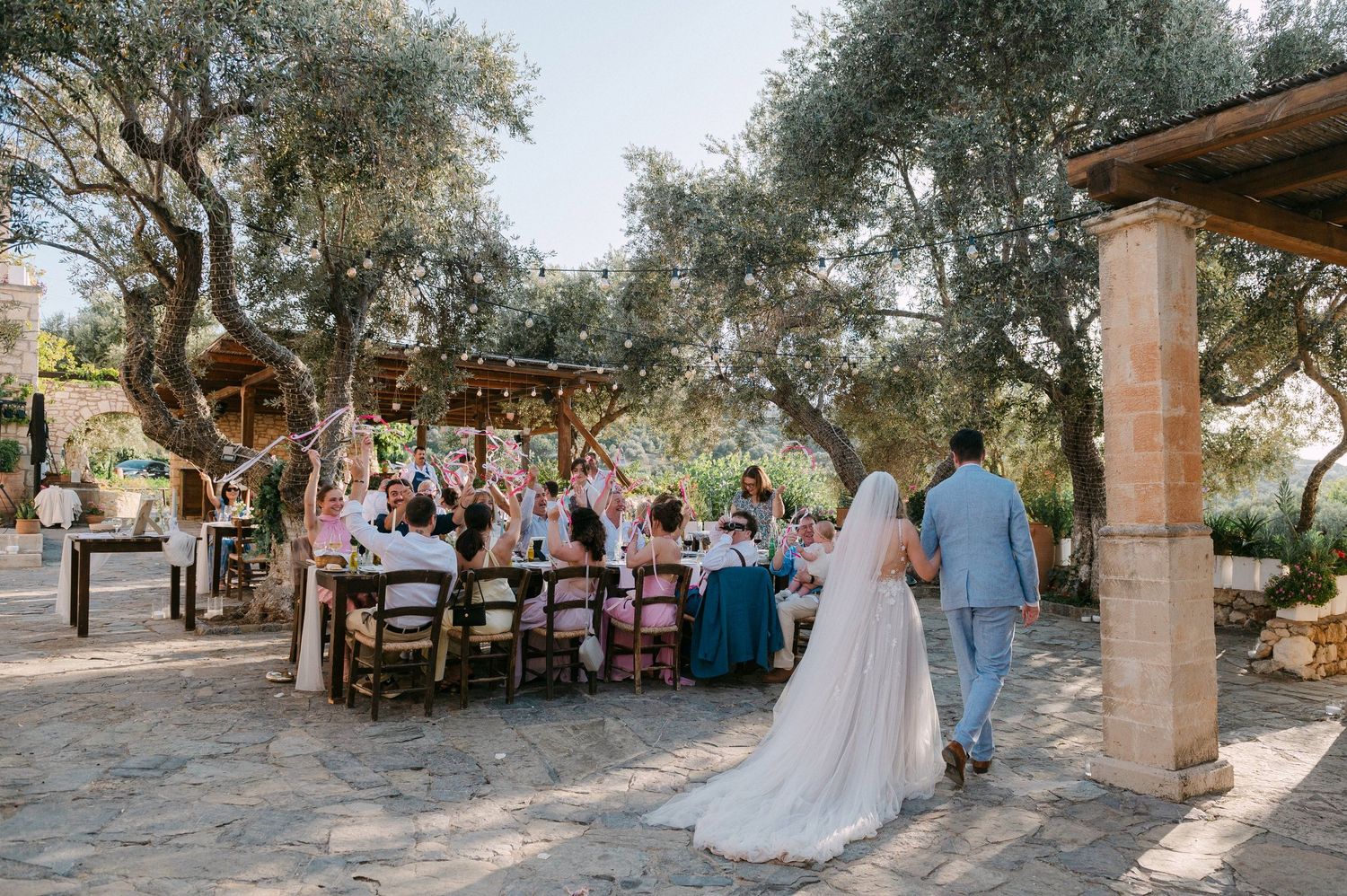 Wedding reception tables and seating arranged outdoors under olive trees at a rustic venue in golden afternoon light.