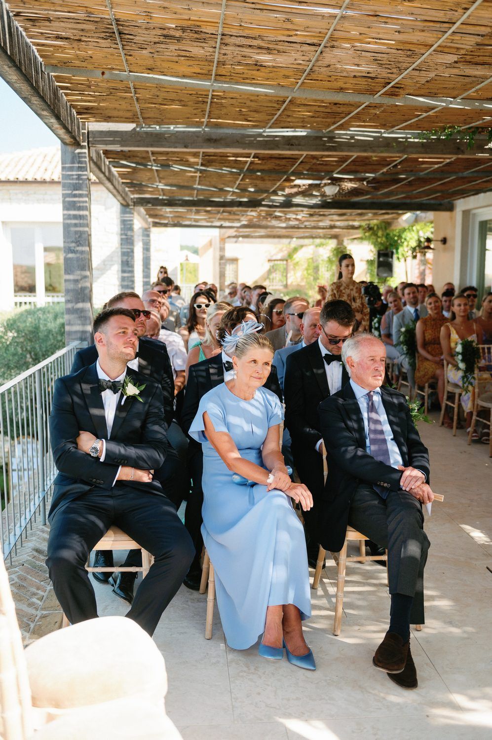 Wedding guests seated under a rustic bamboo ceiling during an outdoor ceremony.