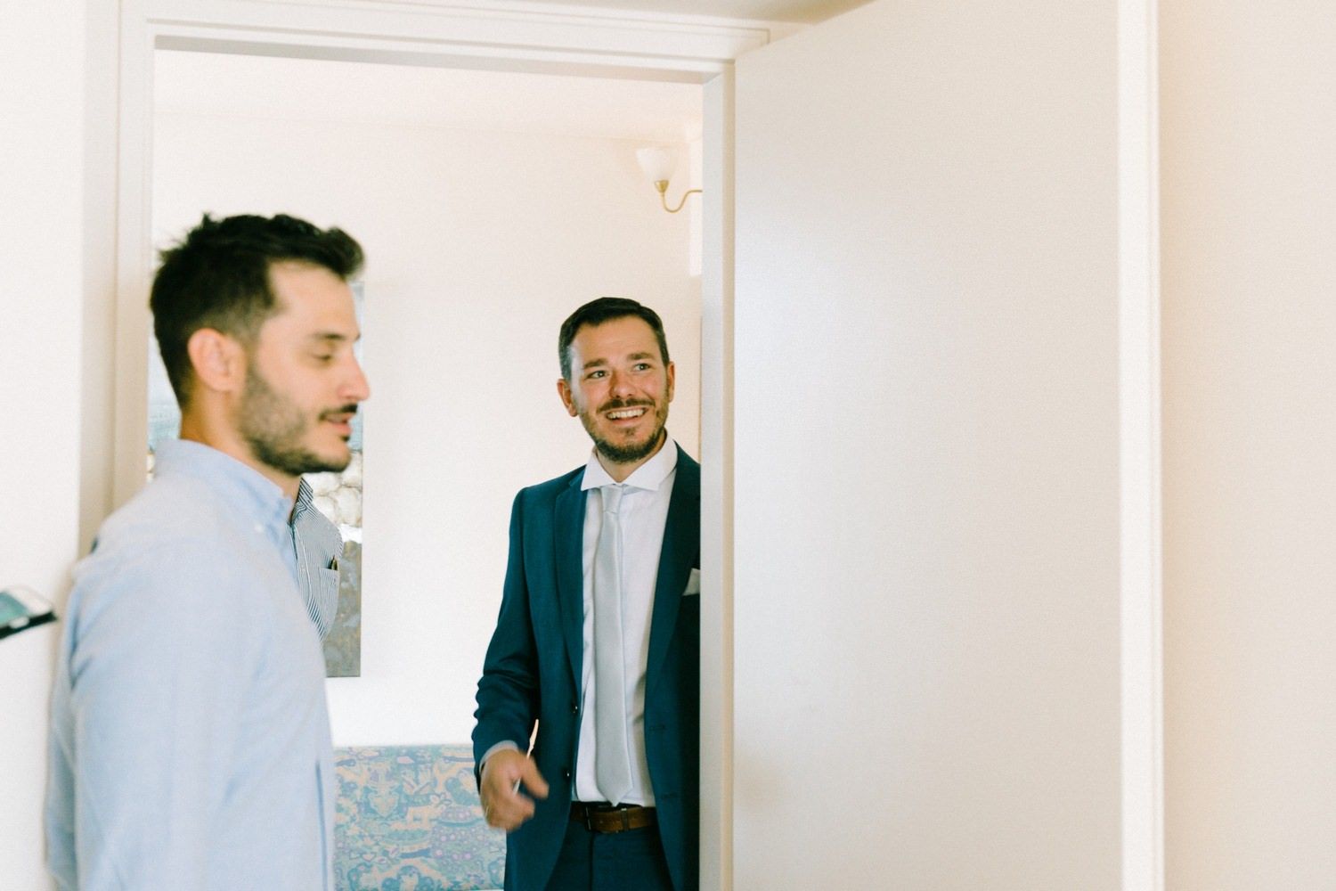 Two people sharing a lighthearted moment in a bright hallway wearing formal attire.